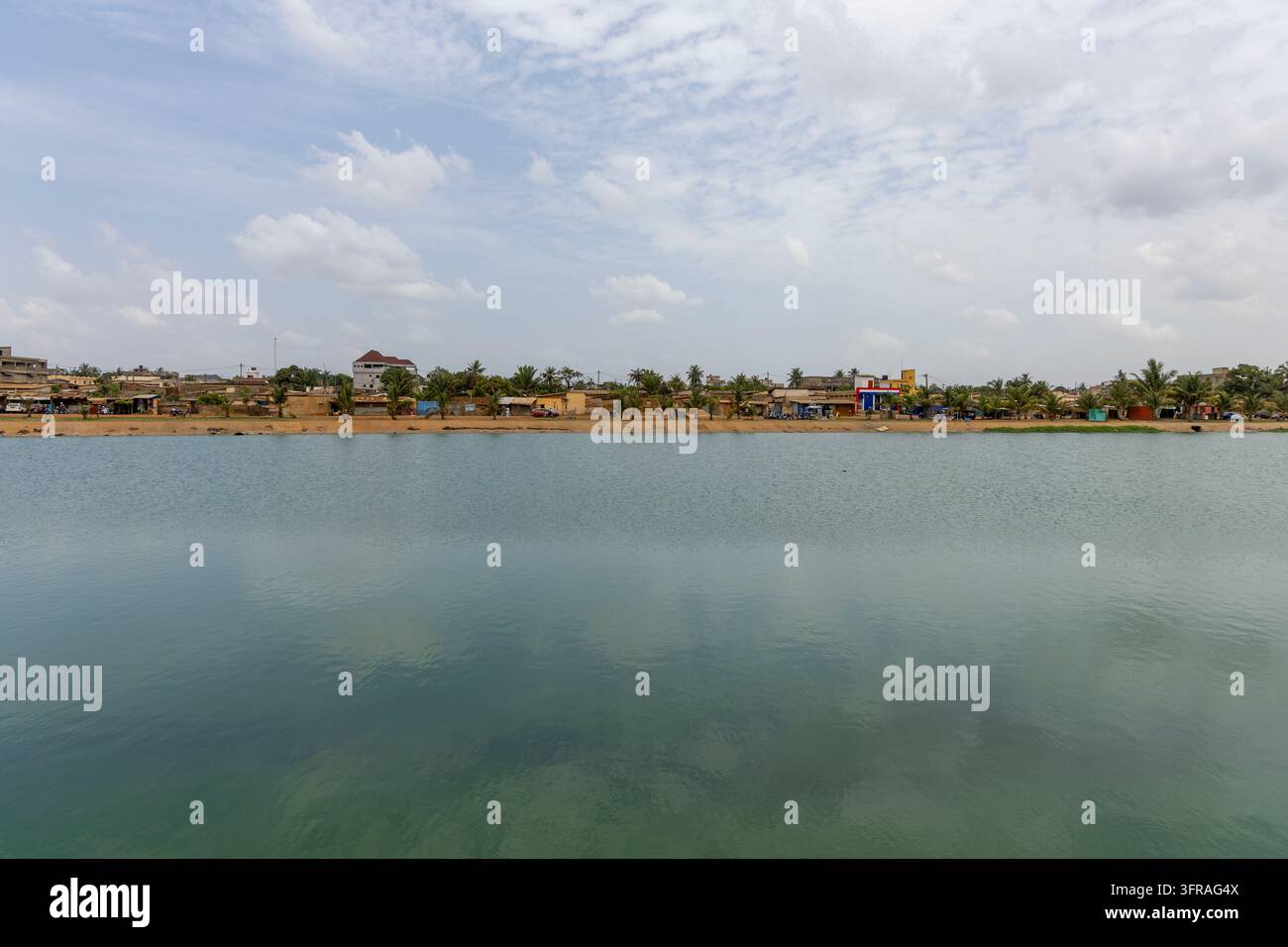 Un lago calmo si estende davanti a un quartiere sul lungomare con palme ed edifici bassi, Regione Marittima, Lomé, Togo Foto Stock