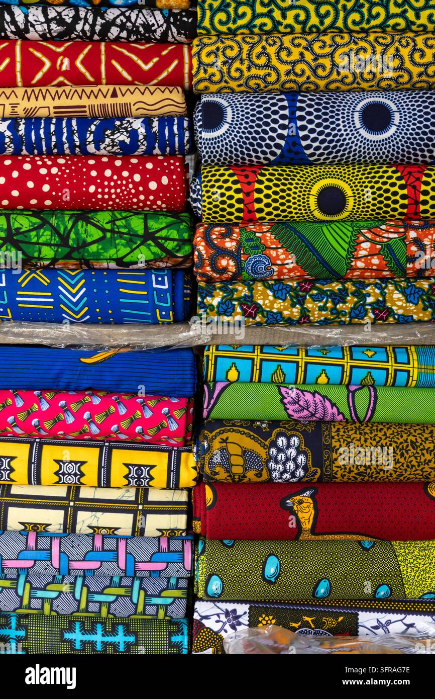 Rotoli di tessuti colorati a stampa cerata sono impilati per la vendita in un mercato, Regione Marittima, Lomé, Togo Foto Stock