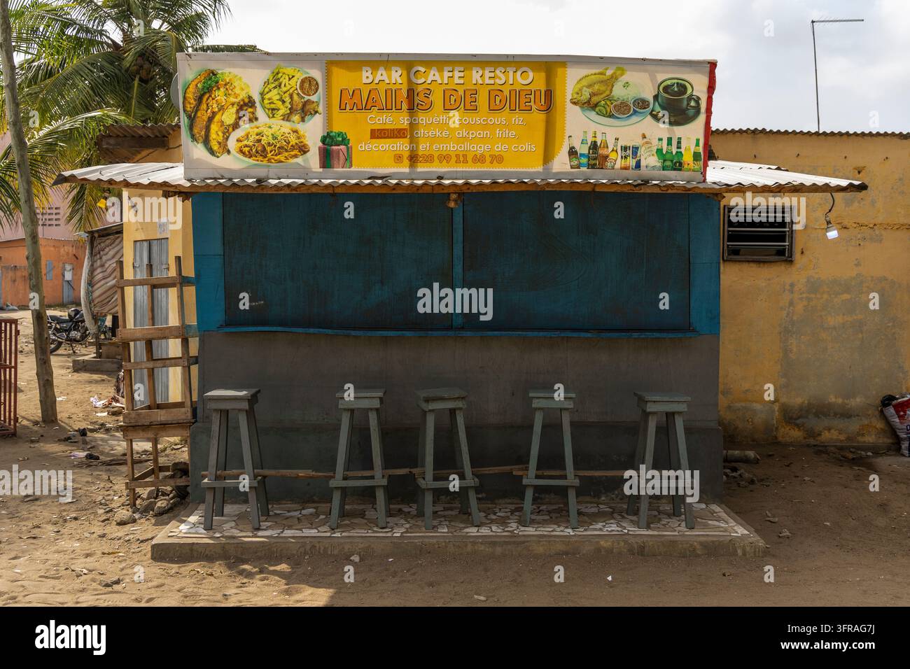 Un banchetto di bar lungo la strada vuoto con sgabelli di legno è chiuso sotto un tetto di lamiera ondulata, Regione Marittima, Lomé, Togo Foto Stock