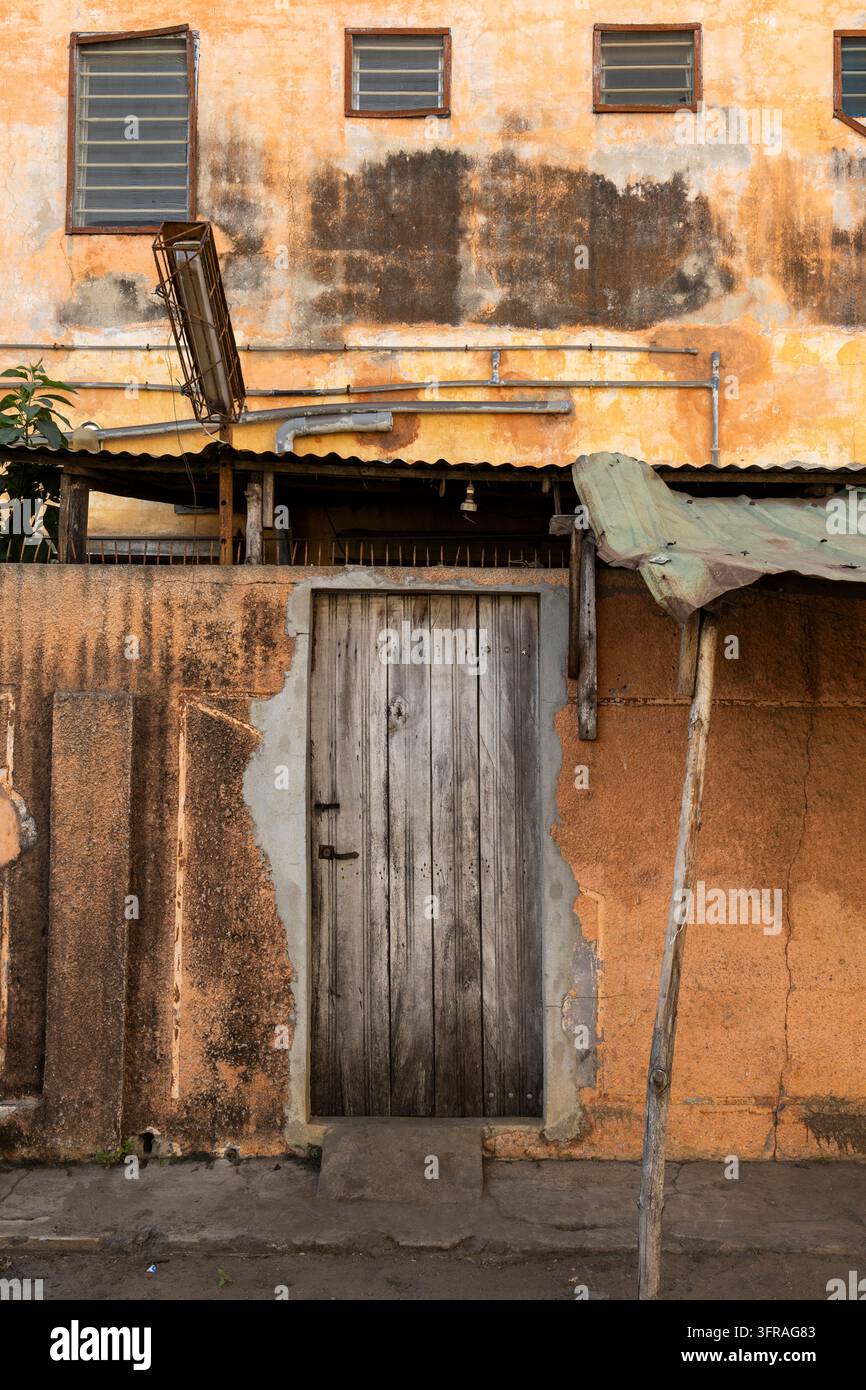 Facciata gialla erosa con una porta di legno e tubi arrugginiti, Regione Marittima, Lome, Togo Foto Stock