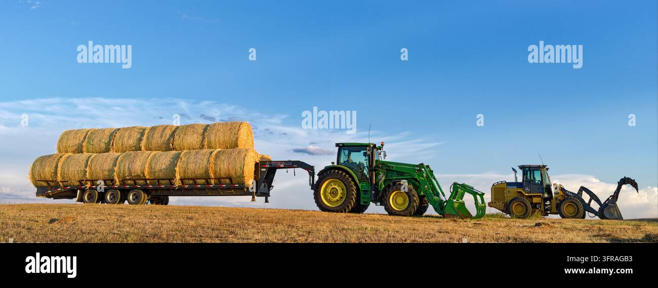 Panorama di trattori John Deere con caricatori e rimorchio pieno di balle di fieno in un ranch del North Dakota, USA Foto Stock
