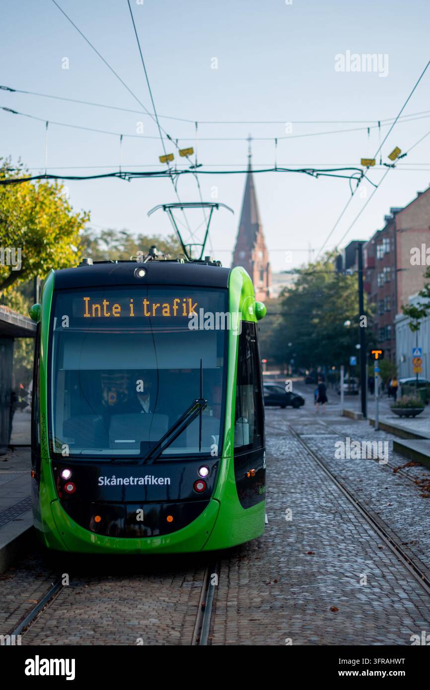 Lund, Svezia – 23 settembre 2024: Tram verde di Skånetrafiken che attraversa il centro di Lund su binari di ciottoli con linee elettriche aeree e histori Foto Stock