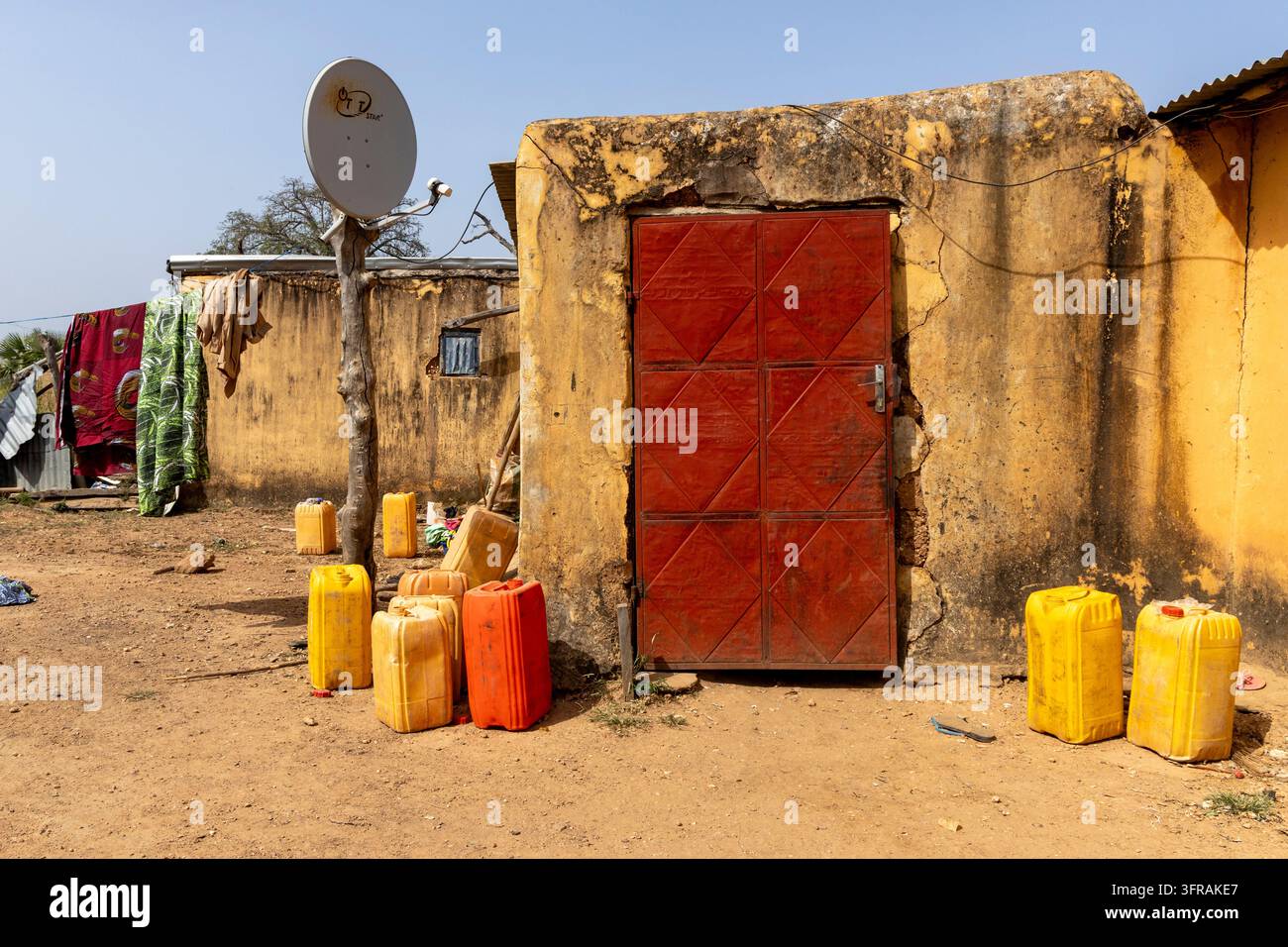 Porta metallica rossa segna l'ingresso a un complesso rurale della tribù Tamberma con taniche e un'antenna satellitare all'esterno, Koutammakou, Tamberma, Togo Foto Stock