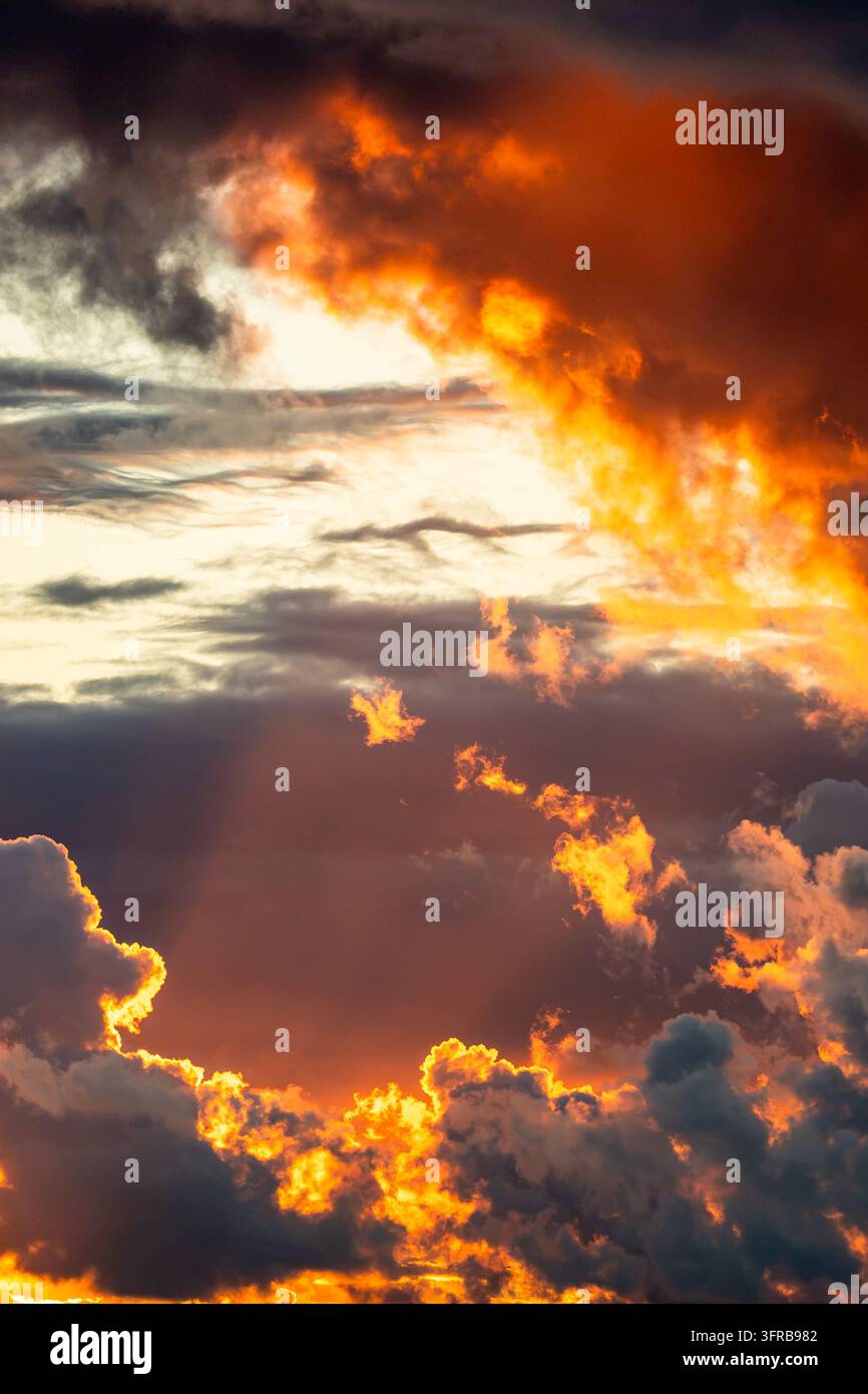 Nuvole di tempesta arancioni infuocate illuminate dal sole al tramonto su uno sfondo di nuvole serali scure e drammatiche Foto Stock