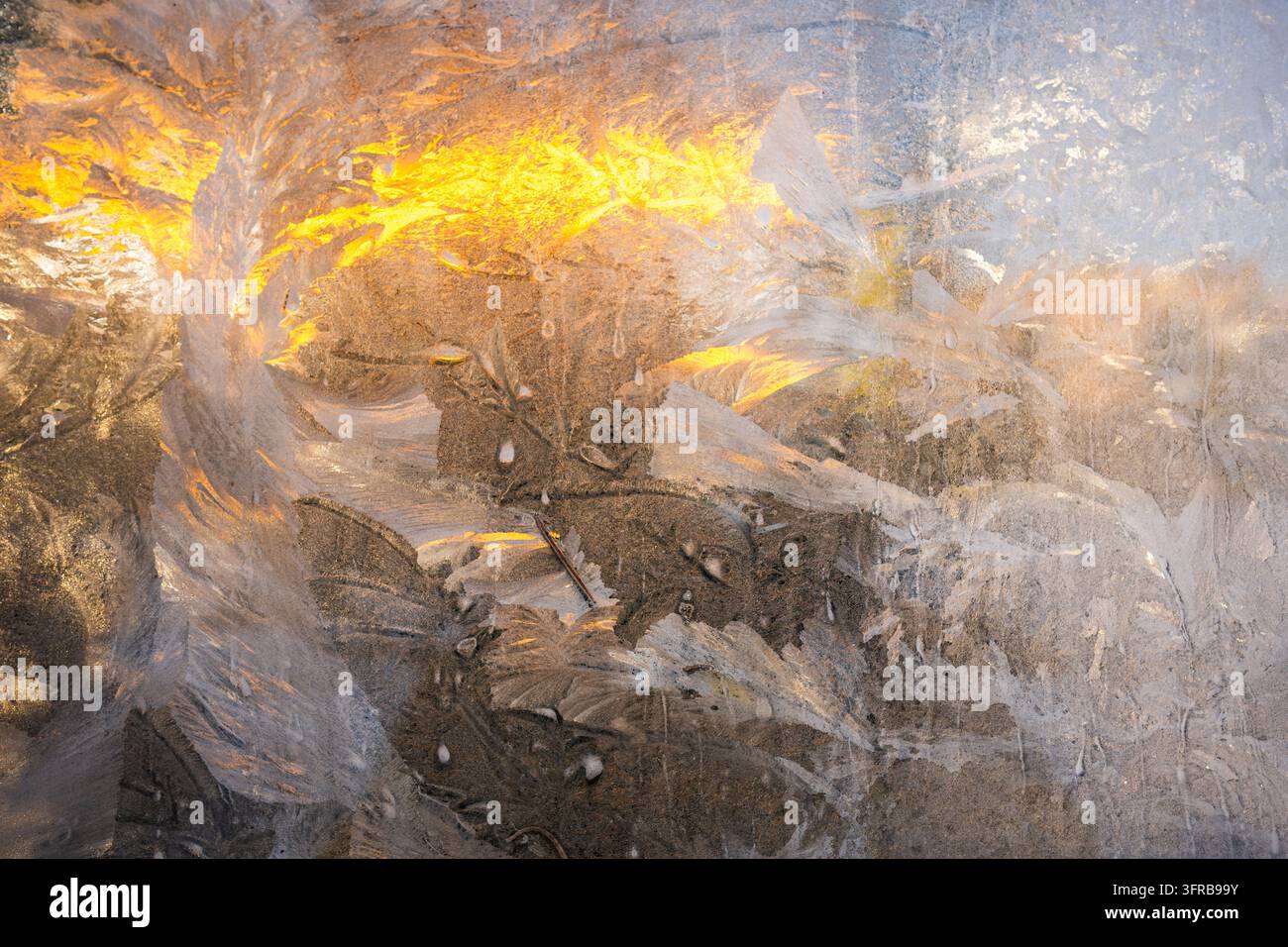 Disegni intricati di ghiaccio coprono il vetro della finestra congelato illuminato dalla calda luce del sole invernale all'aperto Foto Stock