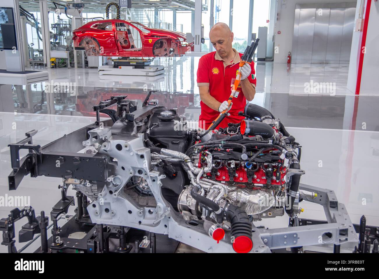 Maranello, Italia – 3 marzo 2025: Un tecnico utilizza uno strumento a manico lungo su un motore e un telaio esposti nella fabbrica Ferrari. Foto Stock