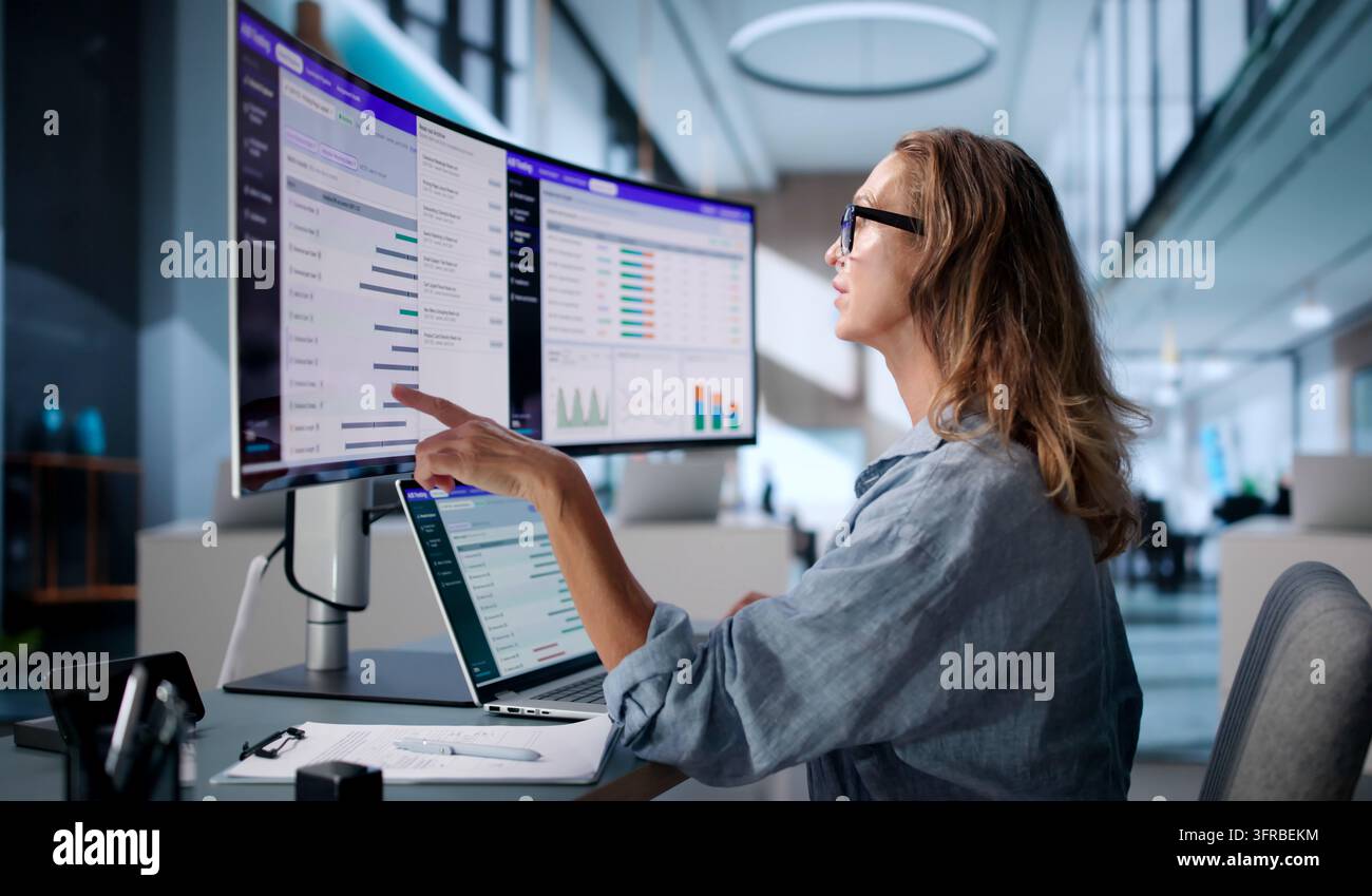 Analista dell'esperienza utente studia i dati del test diviso su uno schermo ultrabreedo con attenzione. Foto Stock