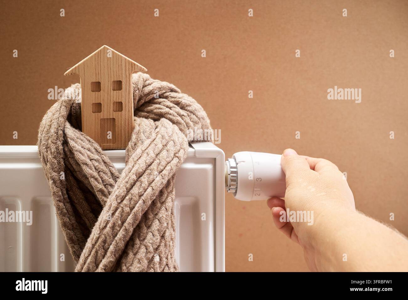 Mano che regola il termostato del radiatore per l'economia del riscaldamento domestico Foto Stock