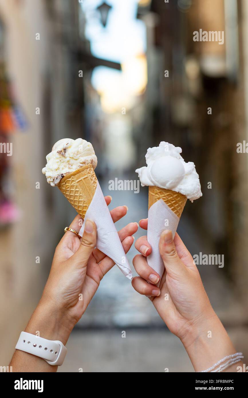 Primo piano di due mani che tengono deliziose palline di gelato cremoso in coni di cialda croccanti all'aperto, dolci prelibatezze estive di gelato su uno sfondo sfocato Foto Stock