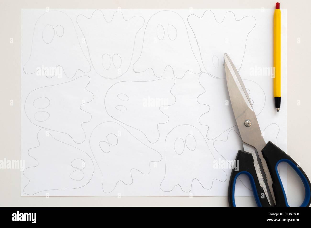 Contorni di fantasmi disegnati su carta bianca. Forbici appoggiate accanto allo schizzo. Una matita gialla è nelle vicinanze. Scena di bricolage per decorazioni di Halloween. Ideale per il fai-da-te hol Foto Stock