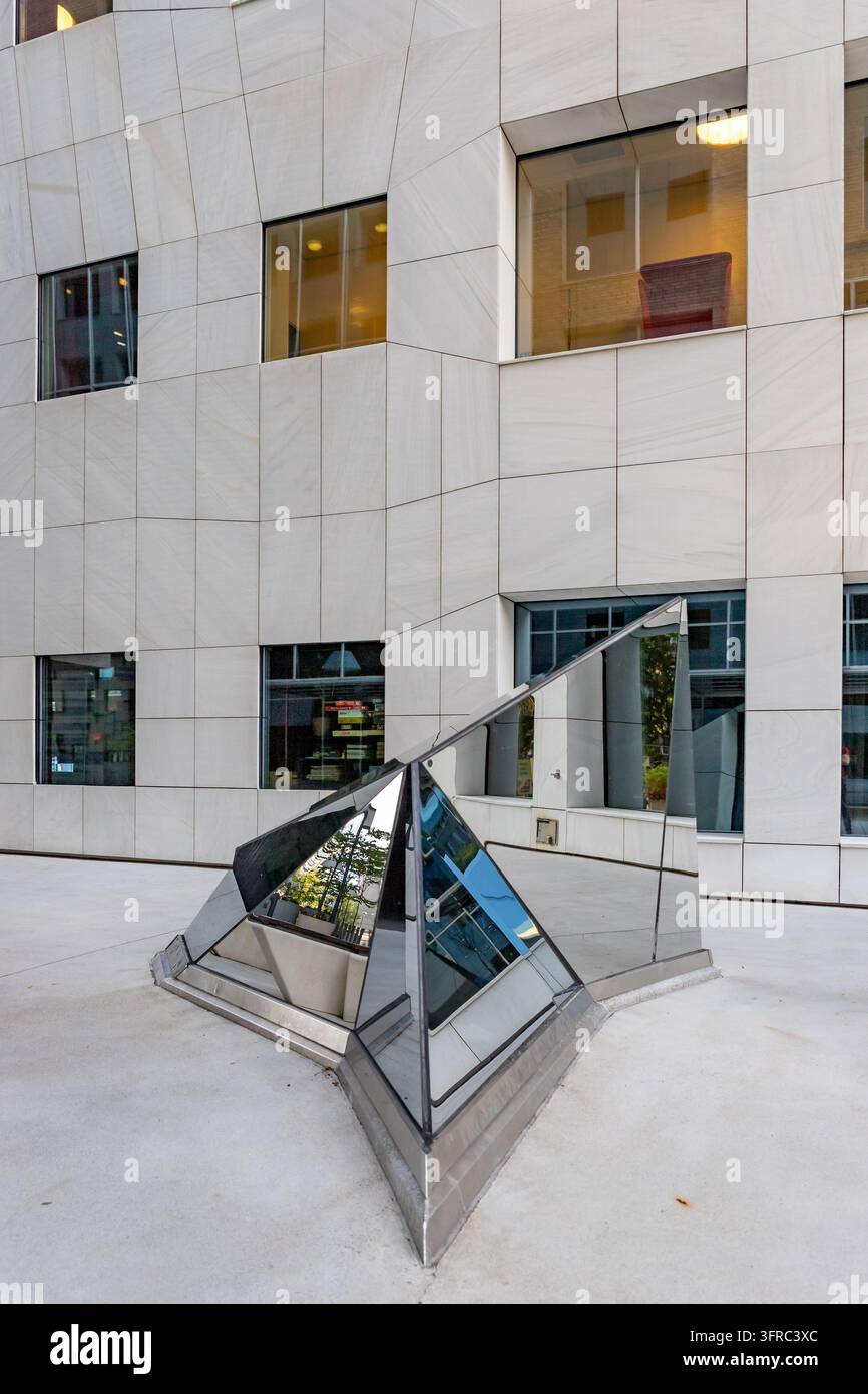 Facciata di un moderno edificio per uffici con finestre quadrate e una scultura geometrica specchiata in un tranquillo cortile urbano Foto Stock