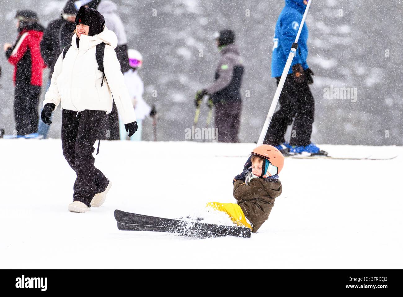 Ruzomberok, Slovacchia – 2 gennaio 2026: Un bambino con casco da sci è seduto nella neve dopo essere caduto mentre utilizzava un teleferico di superficie alla stazione sciistica di Malino Brdo Foto Stock