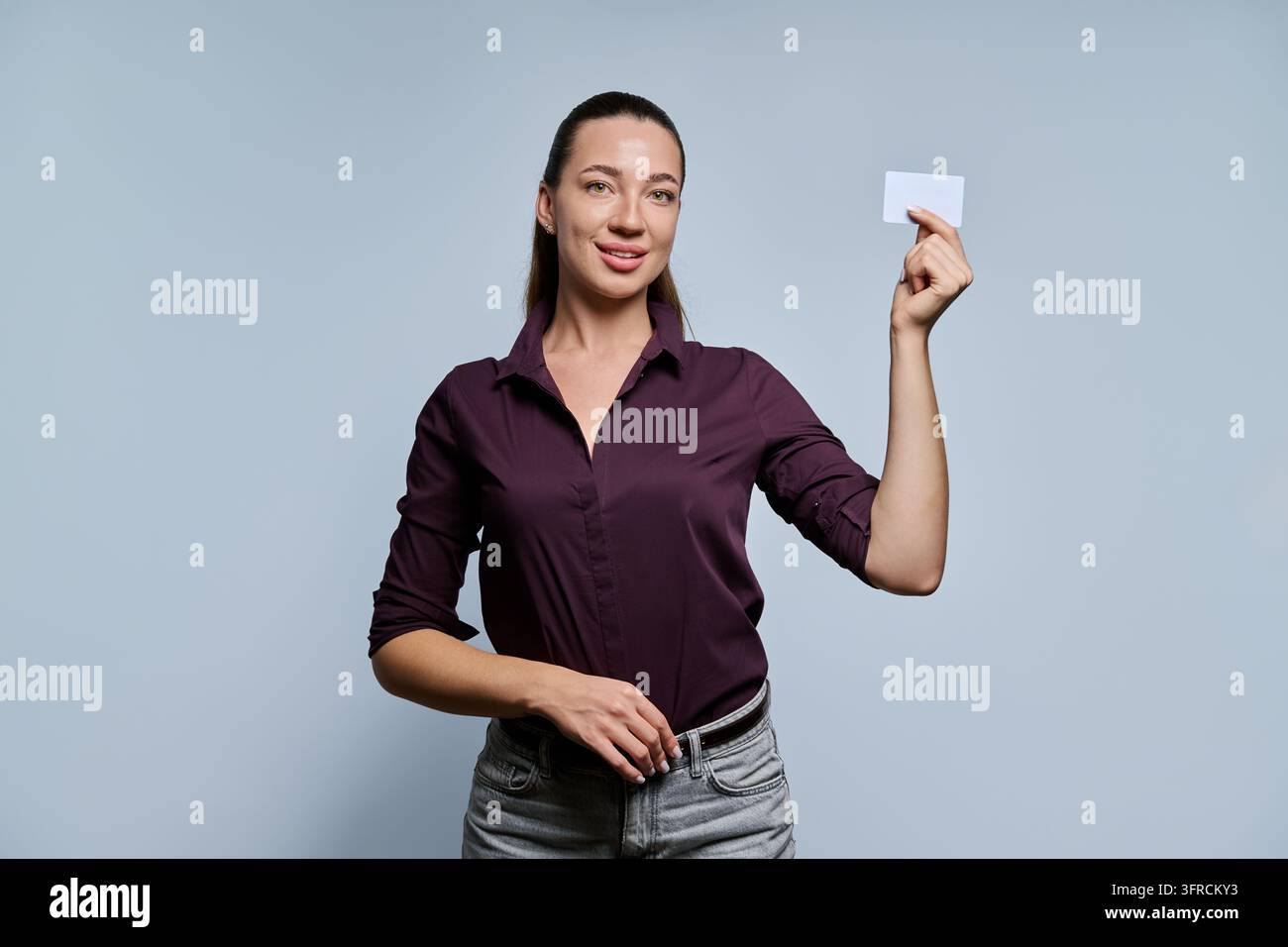 Giovane donna d'affari che tiene una carta di plastica vuota guardando la telecamera su sfondo grigio Foto Stock