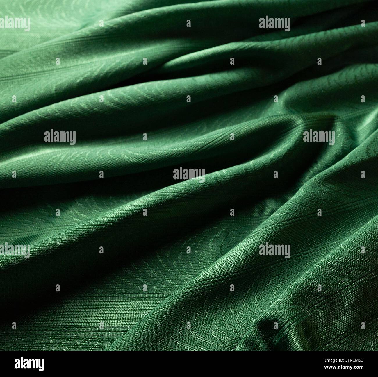 Tessuto drappeggiato verde smeraldo con pieghe diagonali profonde e texture tessile elegante Foto Stock