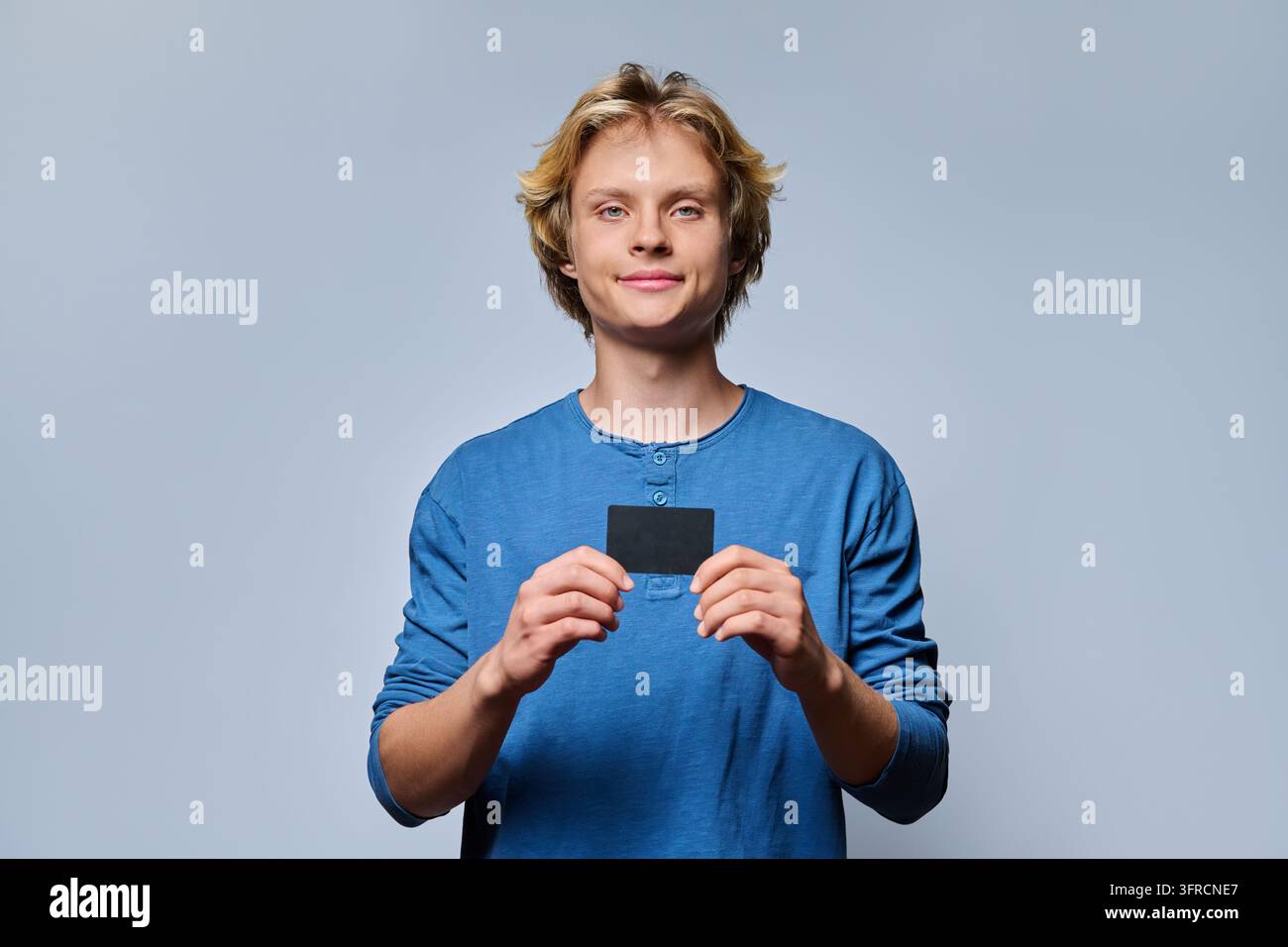 Studente sorridente che tiene un abbonamento nero dei trasporti e guarda la telecamera in studio Foto Stock