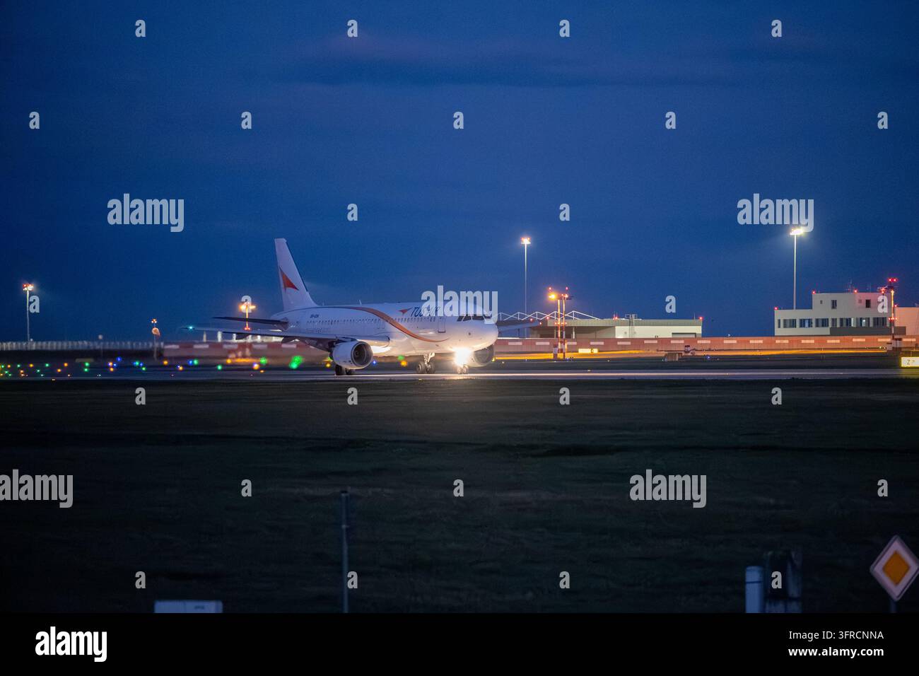 L'Airbus A320 della TUS Airways taxa oltre le luci illuminate dell'aeroporto, con i suoi fari che riflettono sul manto stradale durante l'ora blu. Foto Stock