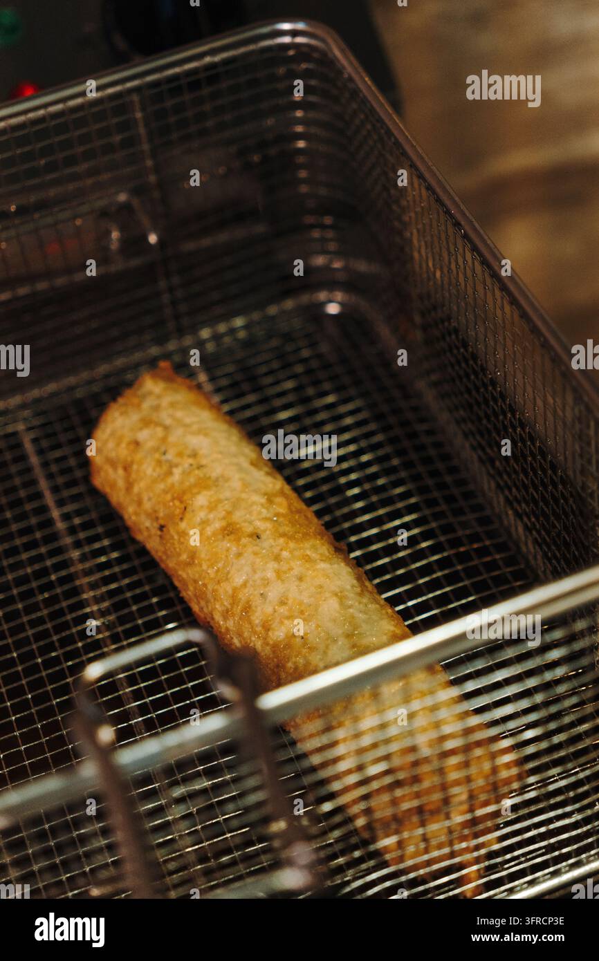 Rollo di sushi dorato e croccante riposto in un cestello di friggere in metallo dopo la frittura. Rappresenta la cucina fusion giapponese, la preparazione di cibi al ristorante e la modalità Foto Stock