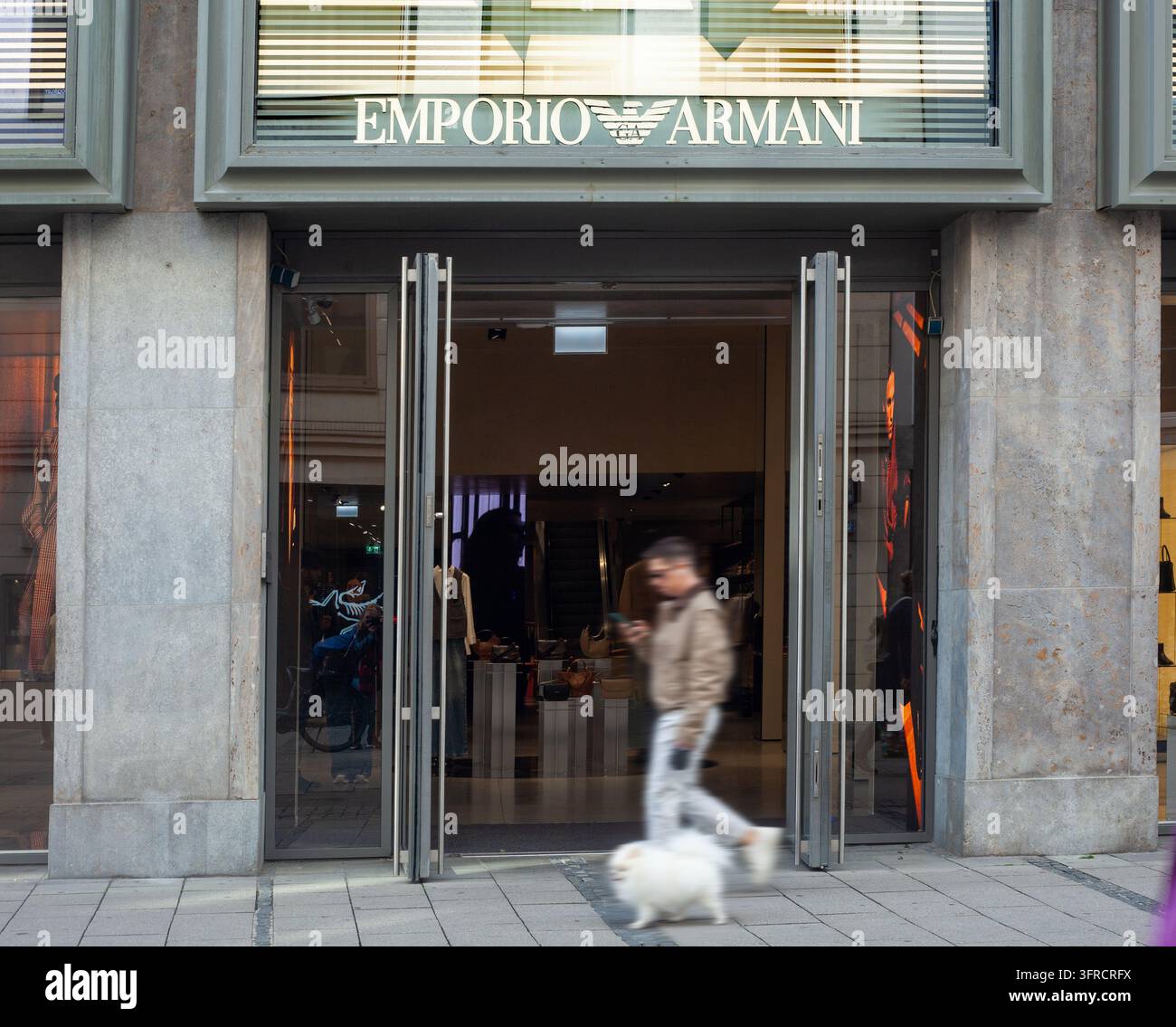 Facciata di cartellone pubblicitario per la moda di lusso Emporio Armani a Monaco di Baviera, passante con cane bianco. Foto Stock