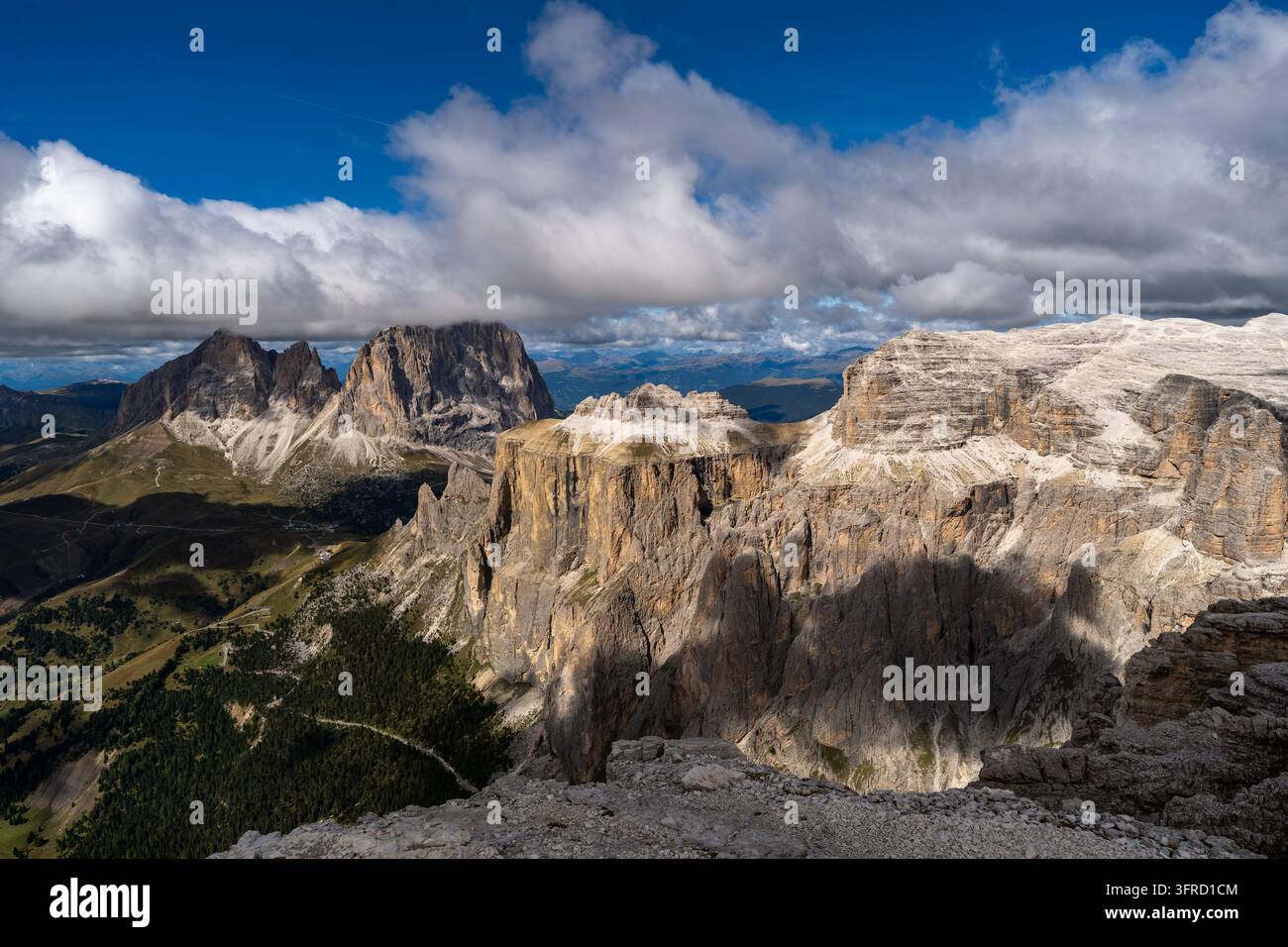 Una vasta veduta ad alta quota di drammatici picchi montuosi e precipizi rocciosi sotto un cielo blu brillante con nuvole bianche nelle Dolomiti, Italia. Macchie s Foto Stock
