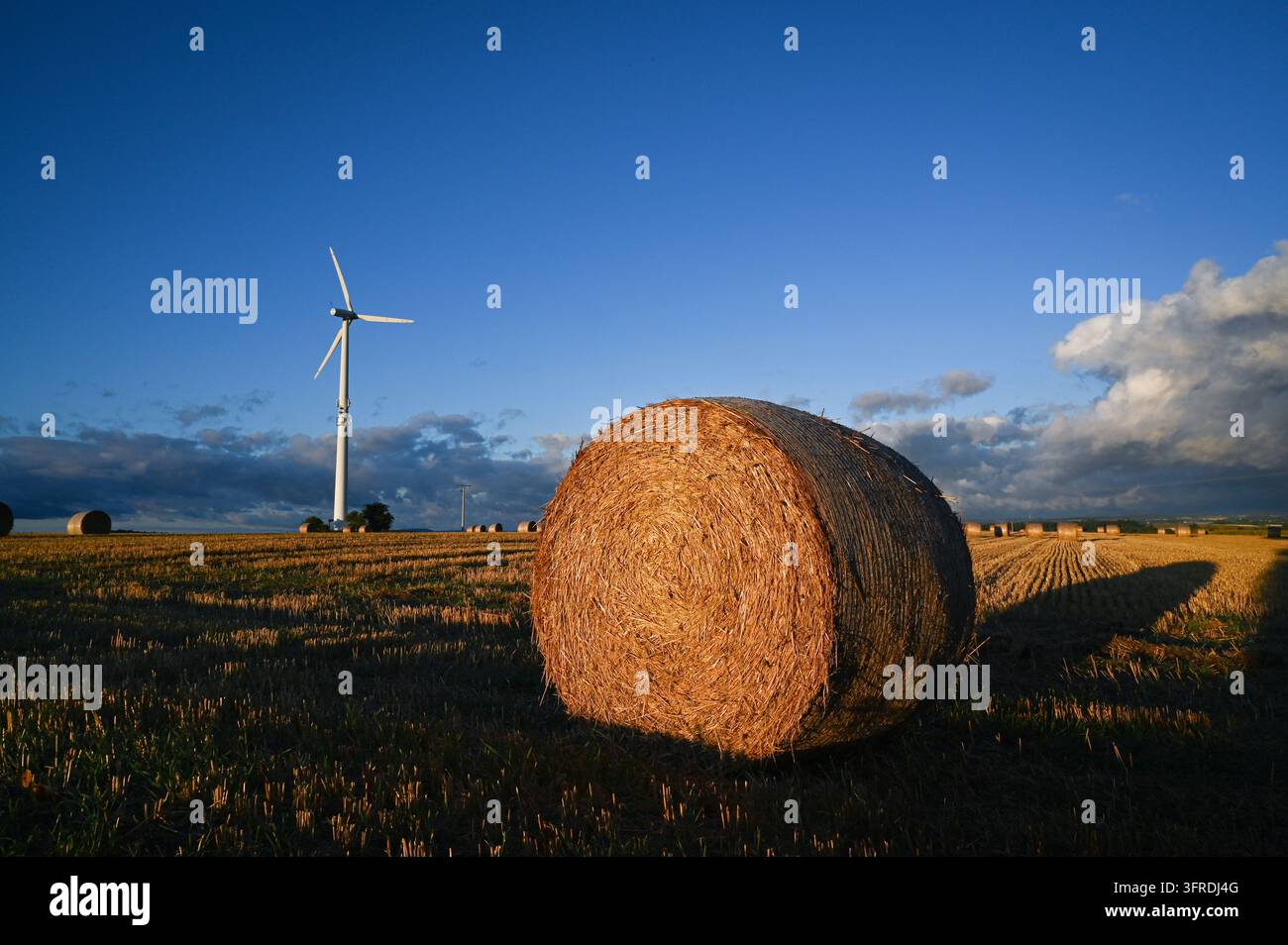 Energia rinnovabile pulita da una turbina eolica in campagna, incastonata tra campi, balle di paglia e terreni agricoli. Foto Stock