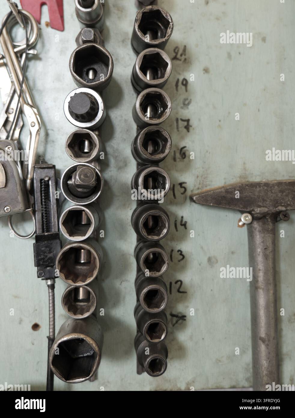 Officina meccanica con un muro che organizza diverse dimensioni di utensili a bussola in metallo, insieme ad altre attrezzature come pinze e un martello, essenziali per Foto Stock