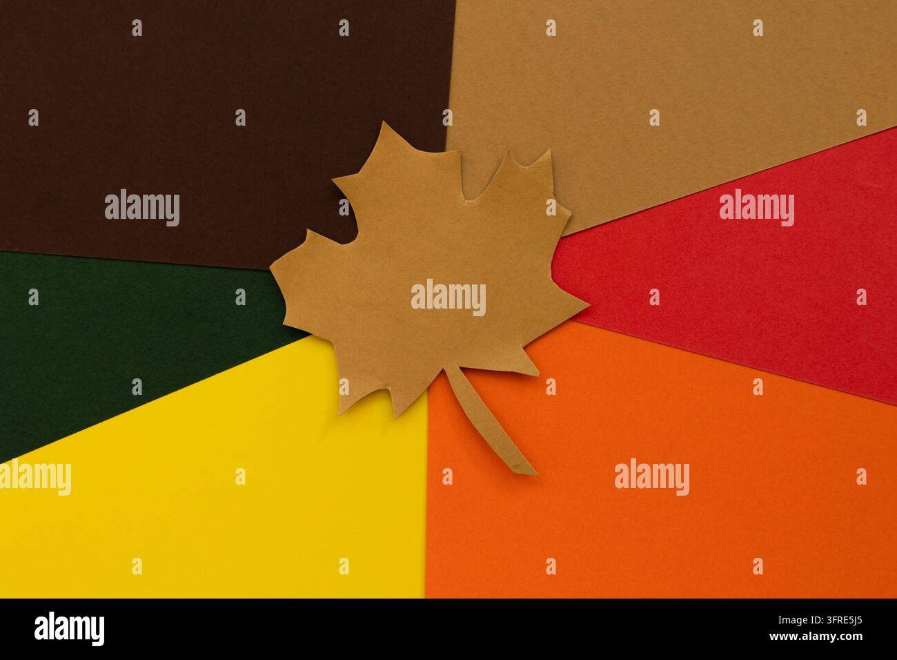 Foglia autunnale fatta di carta su un motivo radiale di foglie di carta in toni caldi, che crea un design stagionale decorativo e creativo Foto Stock