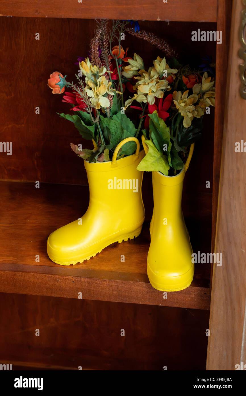 Stivali da pioggia in gomma gialli pieni di tulipani freschi come decorazione autunnale creativa, che uniscono fascino rustico, fiori di stagione, estetica autunnale accogliente e Foto Stock