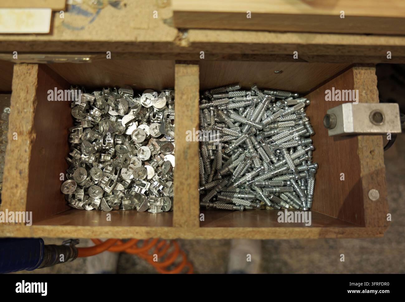 Fissaggi a camma per mobili e tasselli metallici che riempiono scomparti di stoccaggio in legno, rappresentanti componenti essenziali di ferramenta per mobili flat pack Foto Stock