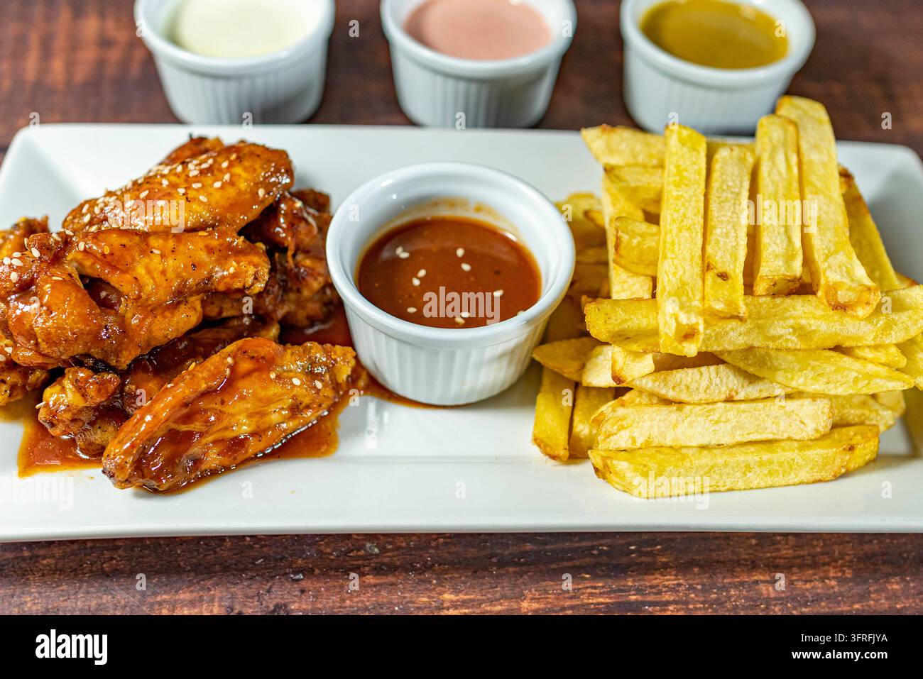 Alette di pollo croccanti glassate con salsa barbecue e servite con patatine fritte, un pasto saporito al ristorante. Foto Stock