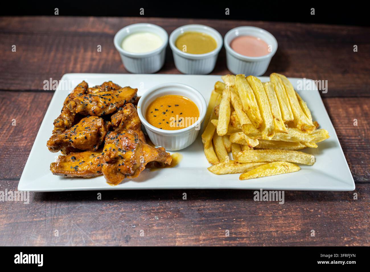 Alette di pollo glassate piccanti con patatine fritte e salse da intingere, antipasto croccante da ristorante pieno di sapori audaci. Foto Stock