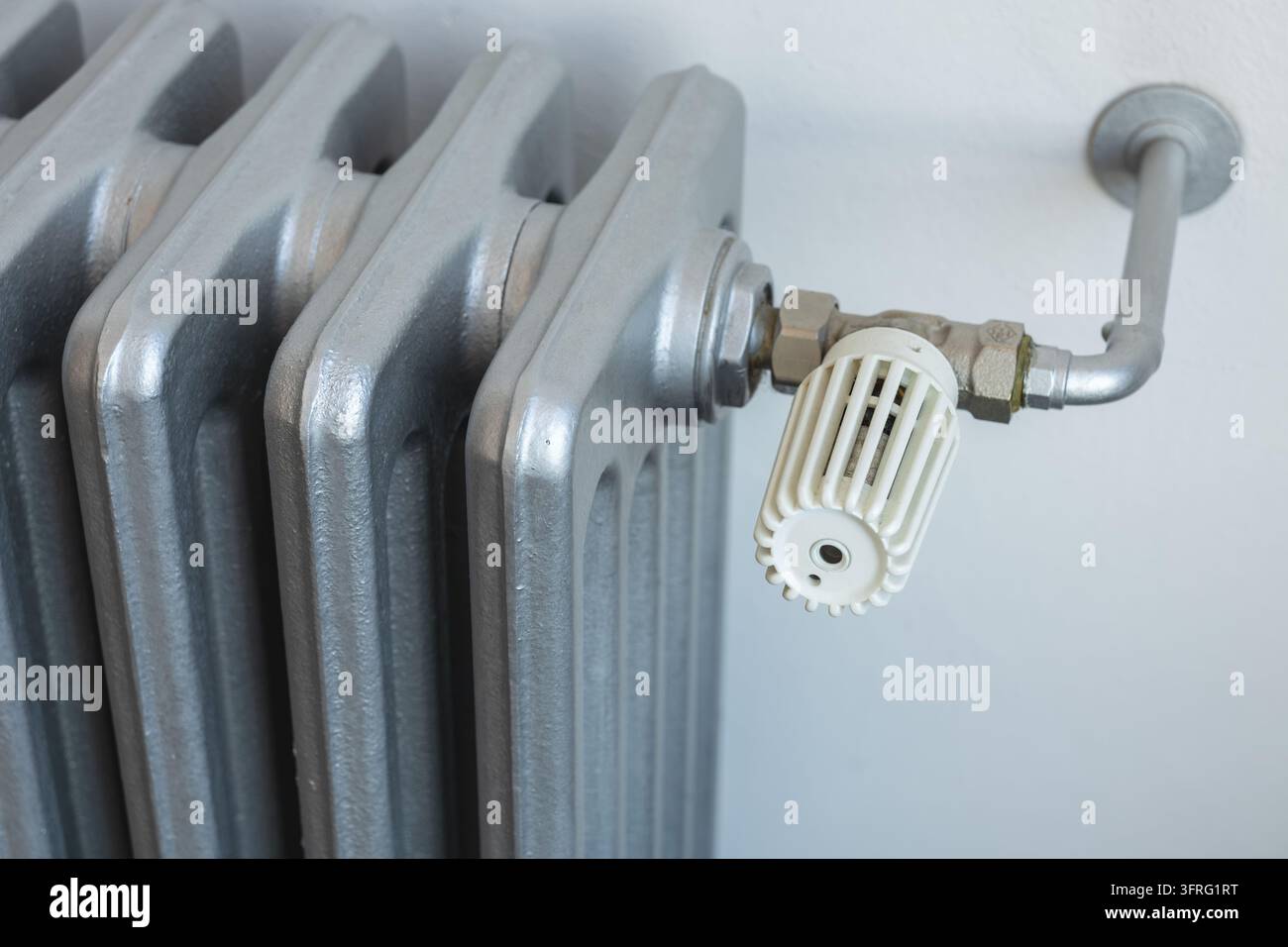 Prima di una valvola di controllo del radiatore bianca collegata a un sistema di riscaldamento tradizionale in ghisa Foto Stock
