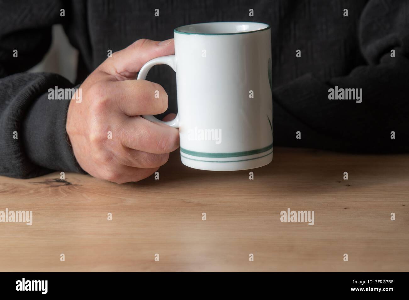 Una tazza di tè tenuta dalla mano di un anziano uomo che indossa una camicia nera. Foto Stock
