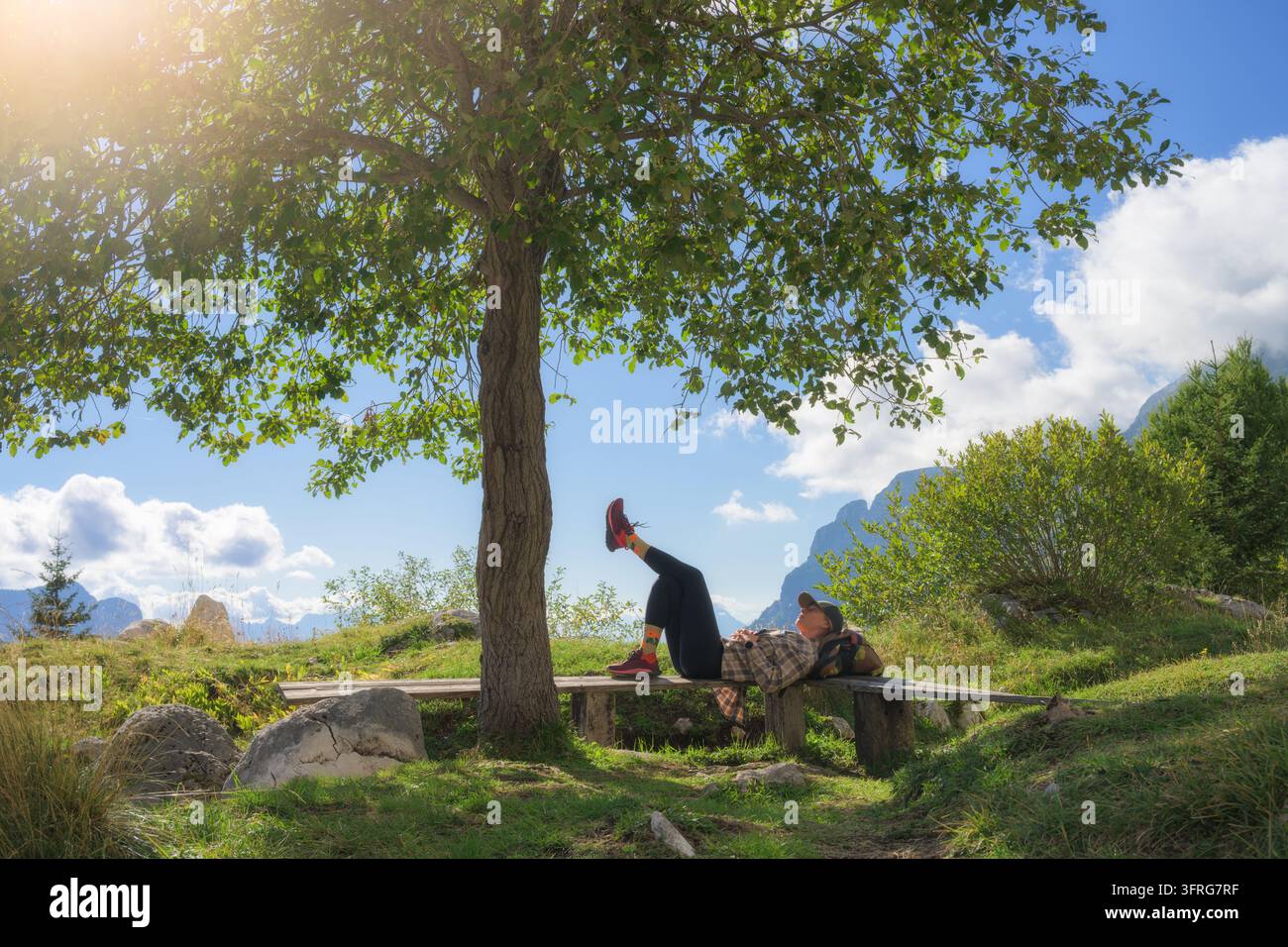 Escursionista donna sdraiata su una panca di legno che riposa sotto un albero verde Foto Stock