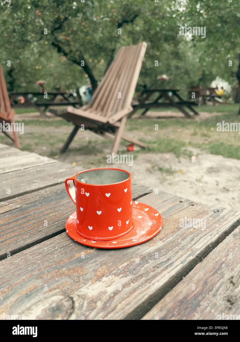 Tazza rossa con motivo a cuore bianco su tavolo di legno in giardino - Immagine stock catturata con smartphone