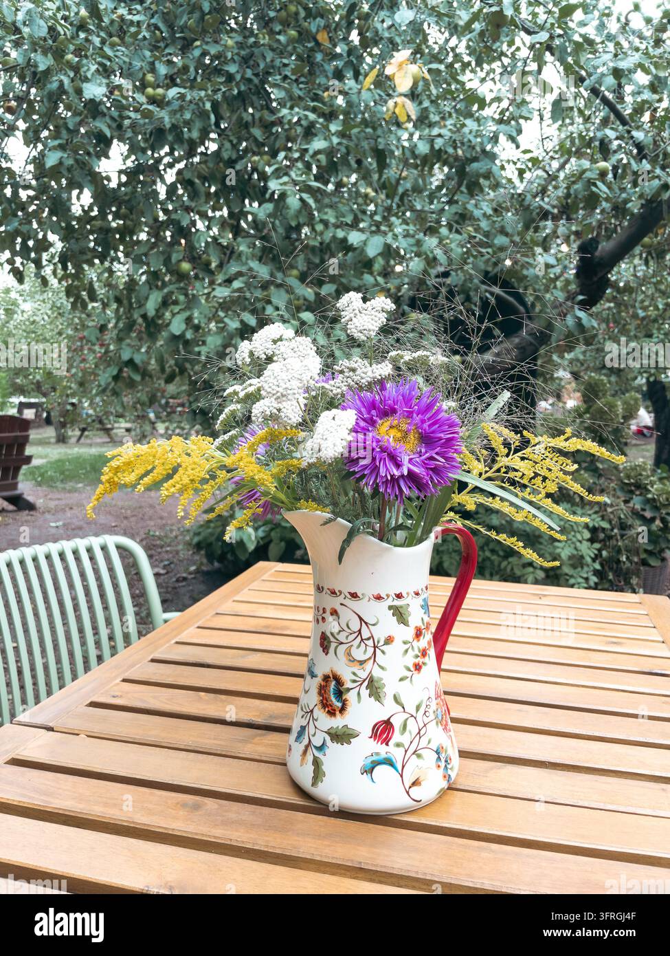Mazzo di fiori selvatici in brocca di ceramica su tavolo di legno in giardino - Immagine stock catturata con smartphone