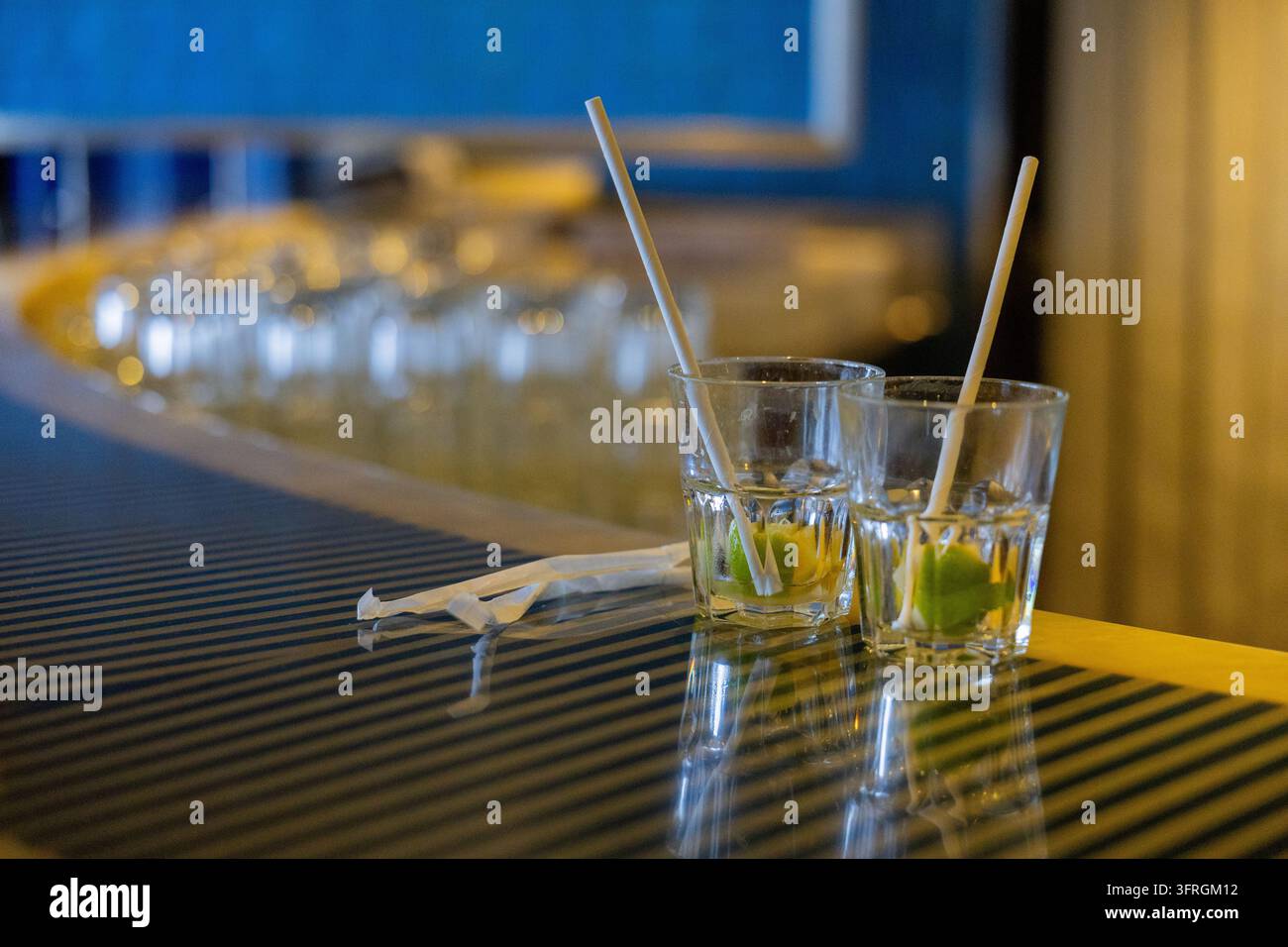 Due bicchieri trasparenti con spicchi di lime e cannucce su un bancone lucido del bar Foto Stock