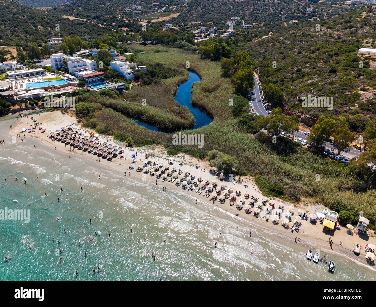 Vista aerea di una sorgente di acqua dolce che entra nel mare oltre una spiaggia sabbiosa con lettini, regione di Agios Nikolaos, isola di Creta nella luce estiva Foto Stock
