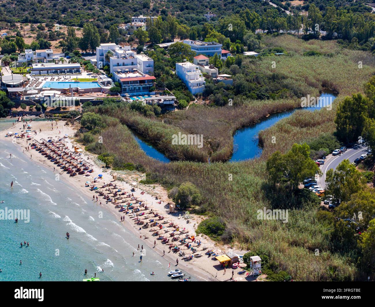 Spiaggia sabbiosa con bagnanti accanto al letto fluviale di una zona umida ad Almyros Beach, Grecia, hotel costieri e colline sullo sfondo in una giornata estiva soleggiata Foto Stock