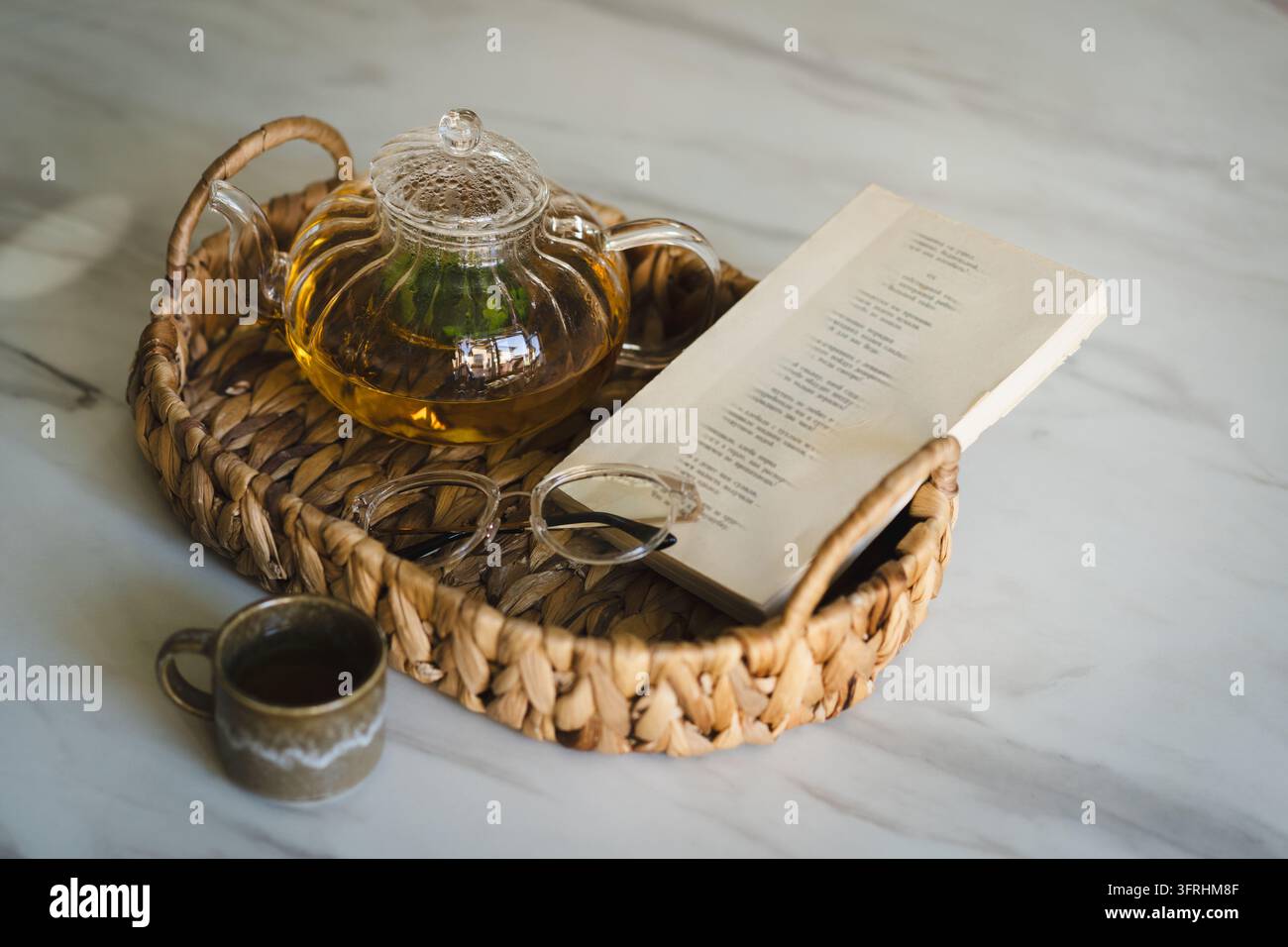 Tè caldo, libro e momento di lettura accogliente in un vassoio di vimini Foto Stock