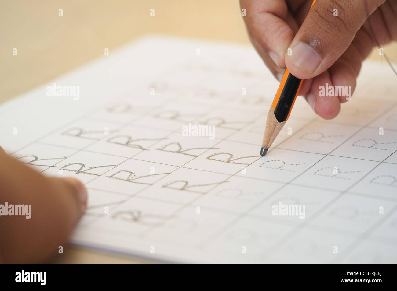 Praticare la scrittura delle lettere su un foglio di lavoro con una matita in un contesto di aula Foto Stock