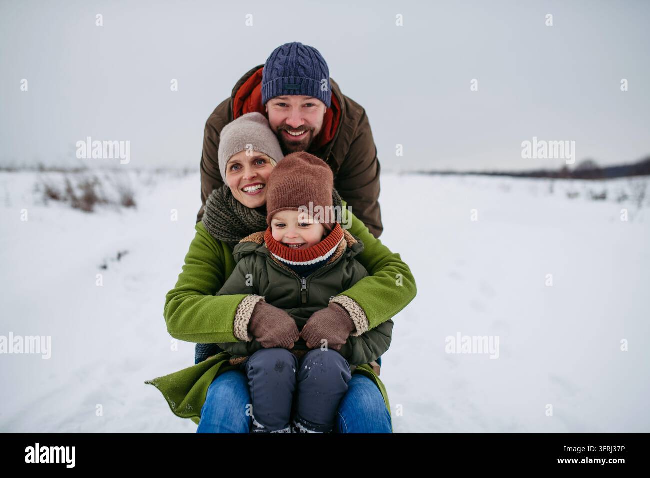 Famiglia felice che si diverte a fare slitta insieme nella campagna innevata invernale. Foto Stock