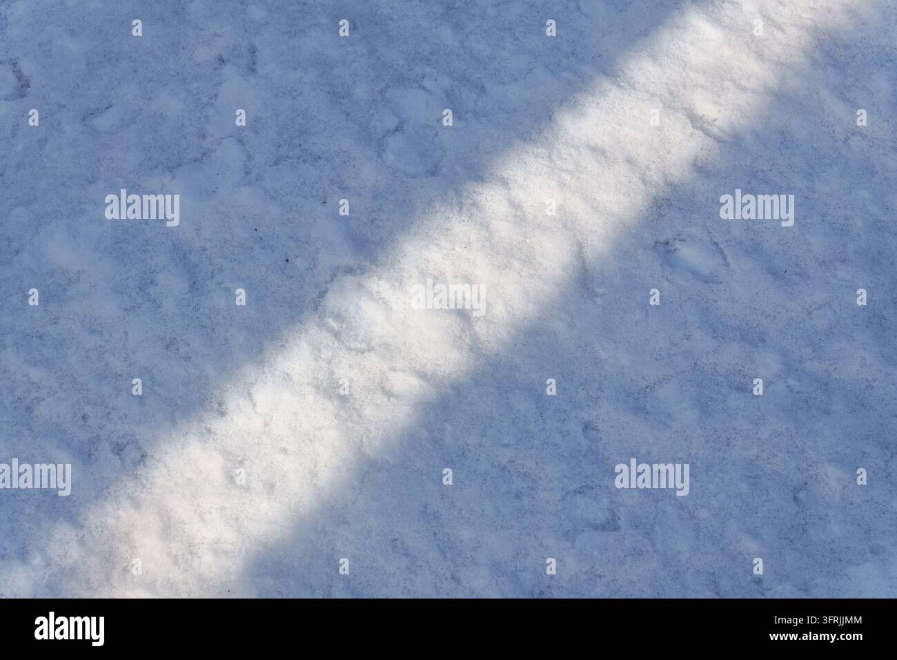 Una banda diagonale di luce solare attraversa il terreno innevato Foto Stock