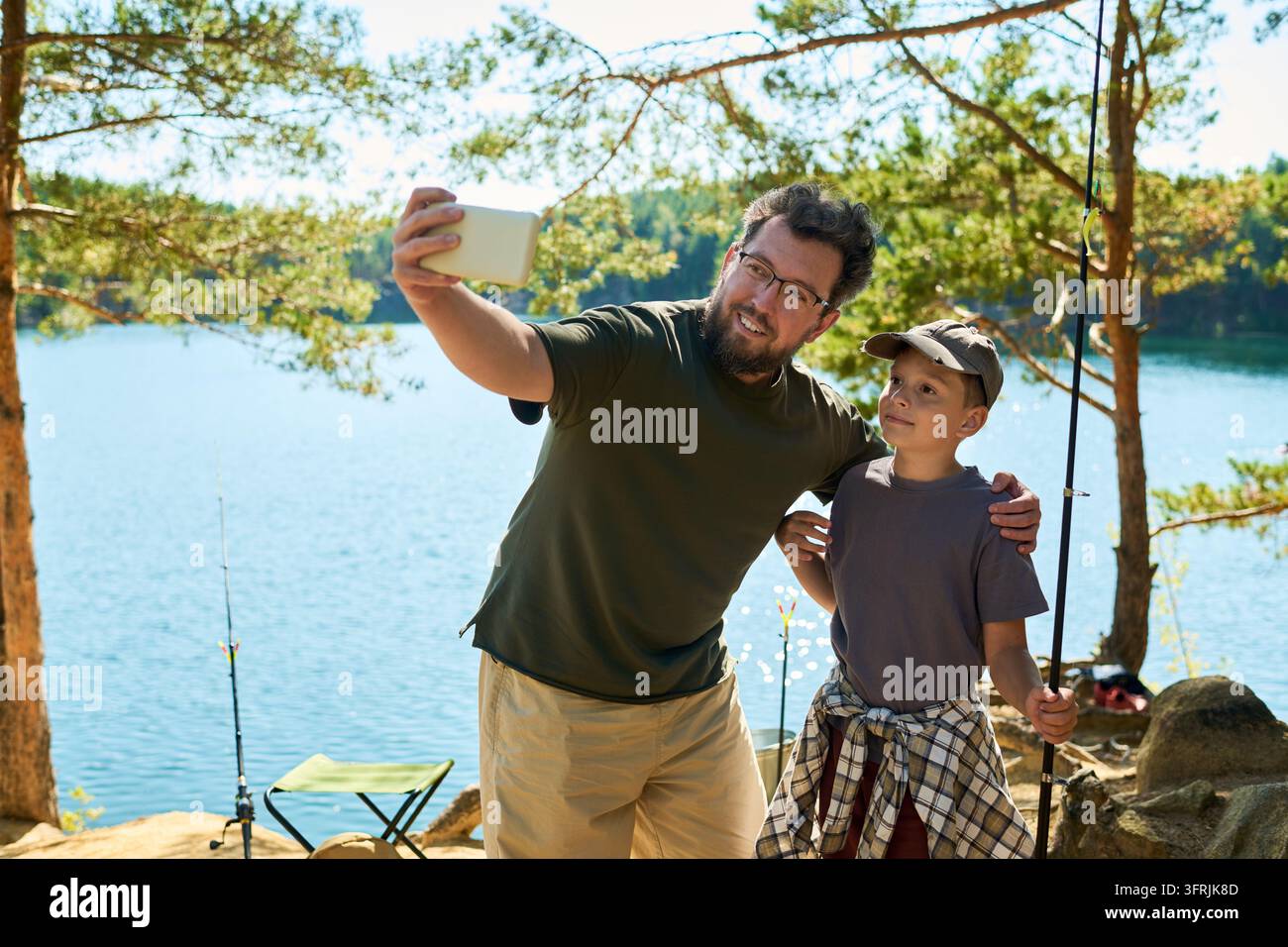 Padre e ragazzo che fanno un selfie con lo smartphone mentre pescano Foto Stock