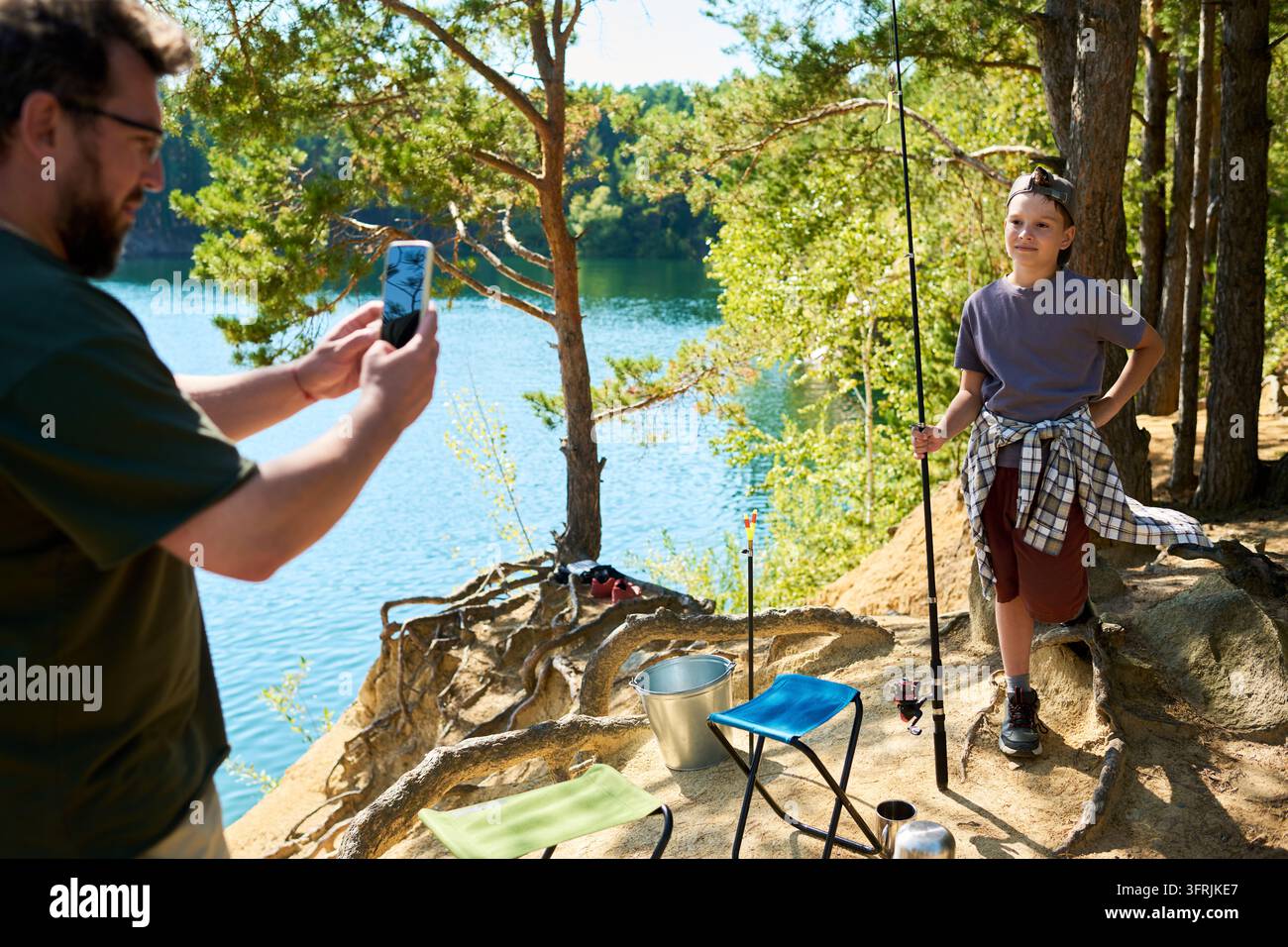 Uomo che scatta una foto con lo smartphone di un ragazzo che pesca al lago Foto Stock