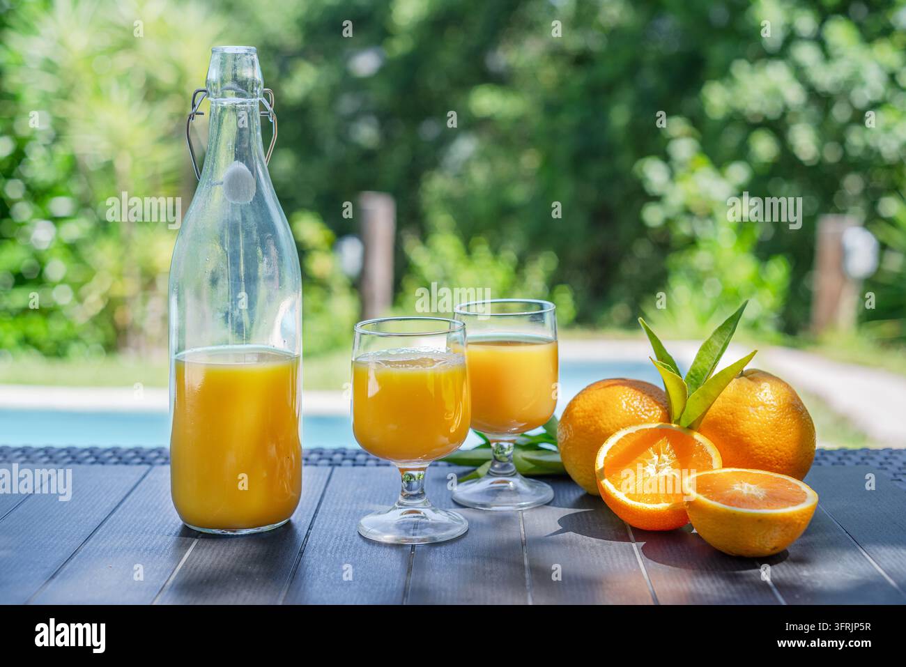 Brocca e bicchieri di succo d'arancia fresco con arance intere vicino a una piscina all'aperto. Foto Stock