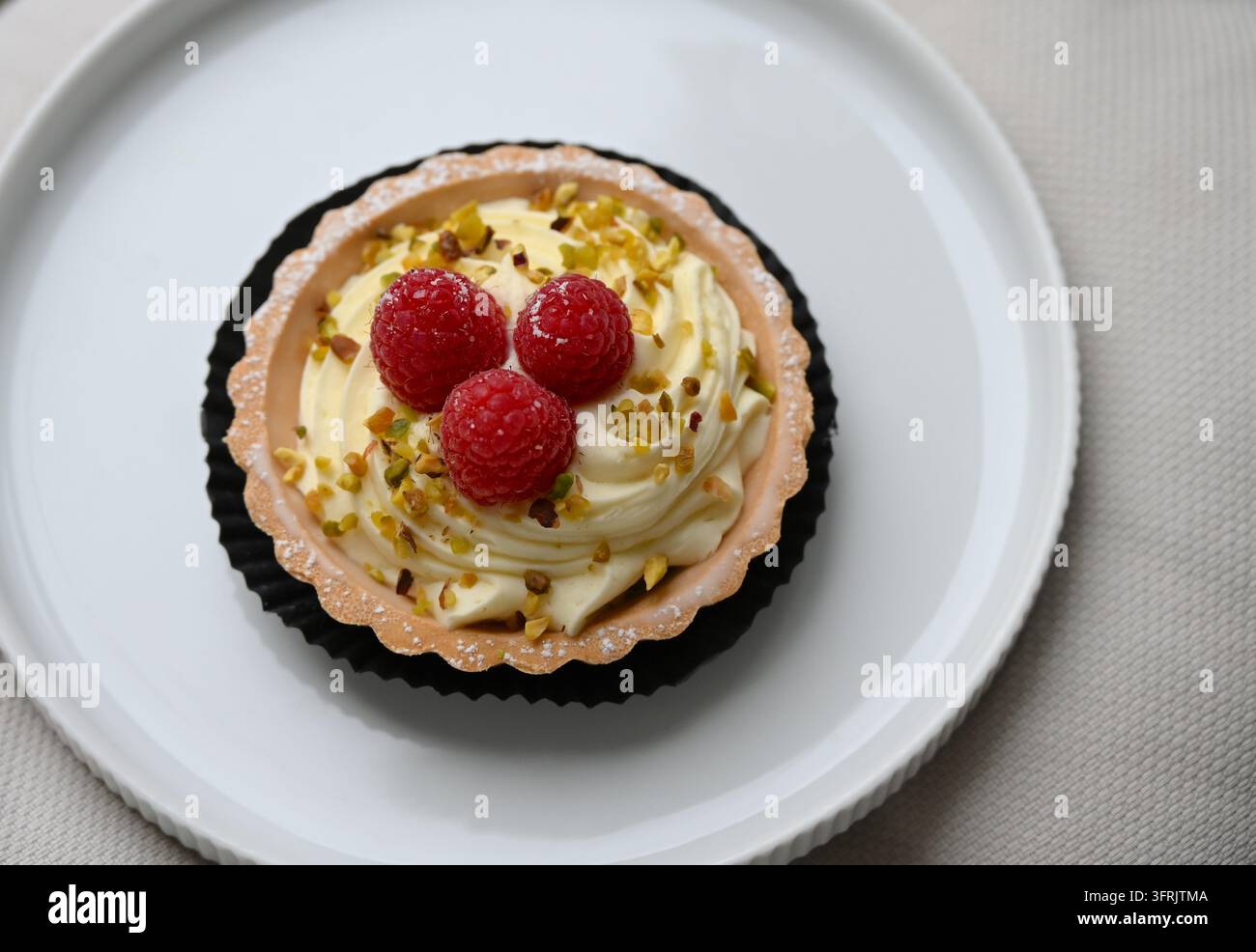 Tartina stupenda ai lamponi e pistacchi su un piatto di ceramica bianca. Foto Stock