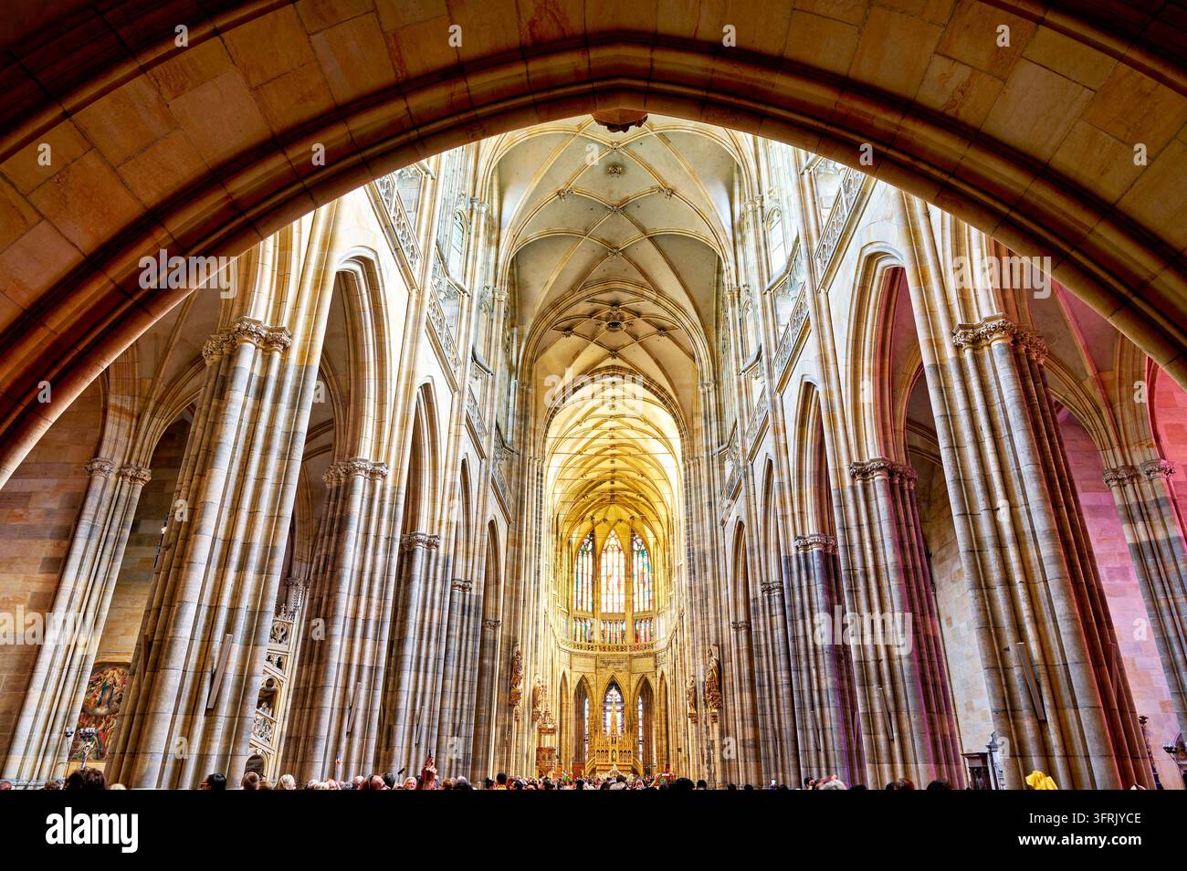 Visitatori nella navata gotica della Cattedrale di San Vito al Castello di Praga, incorniciati da un arco di pietra, con volte a costoloni e finestre di vetro colorato. Foto Stock