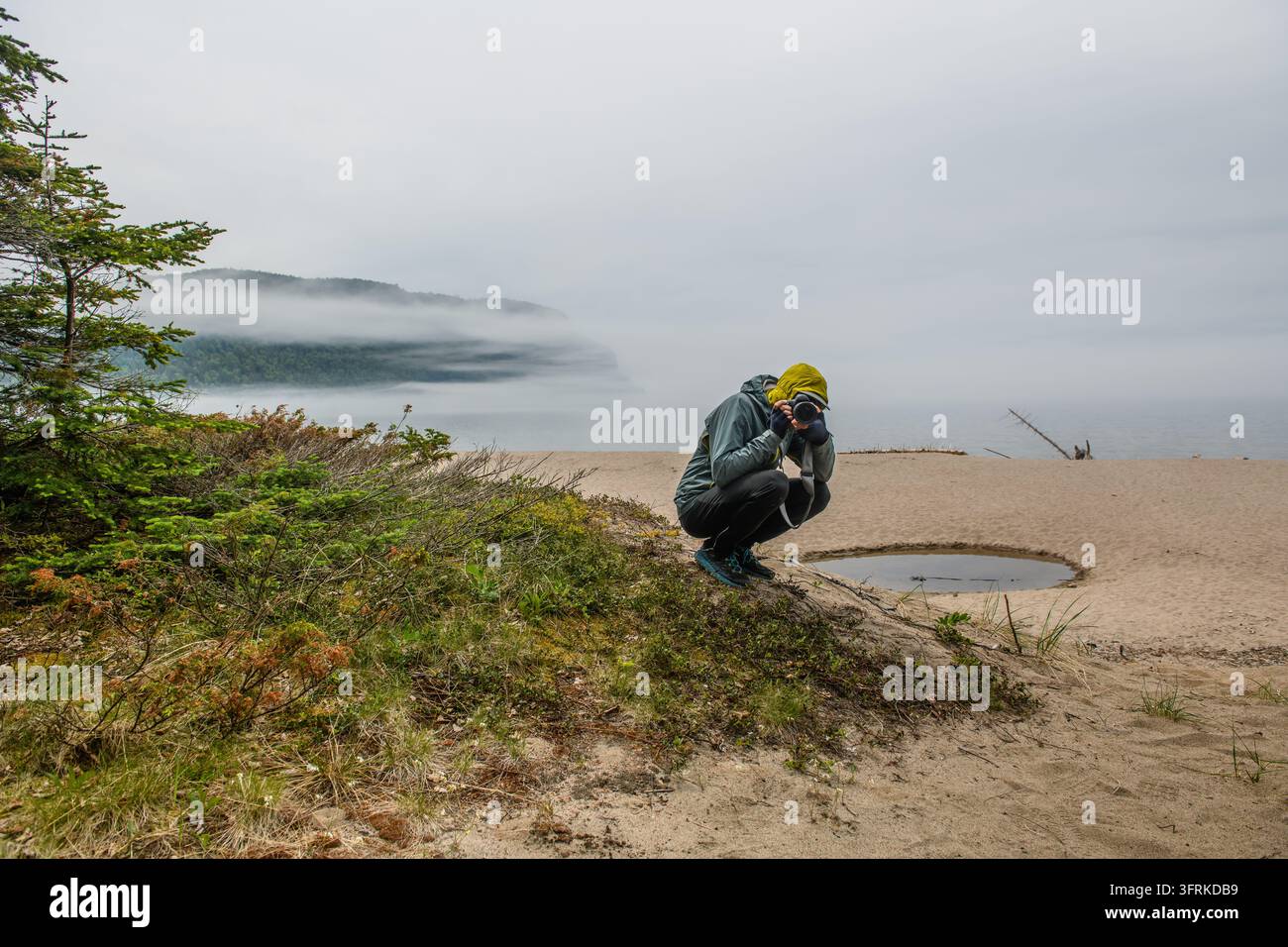 Fotografo che cattura un paesaggio nebbioso da una riva sabbiosa Foto Stock