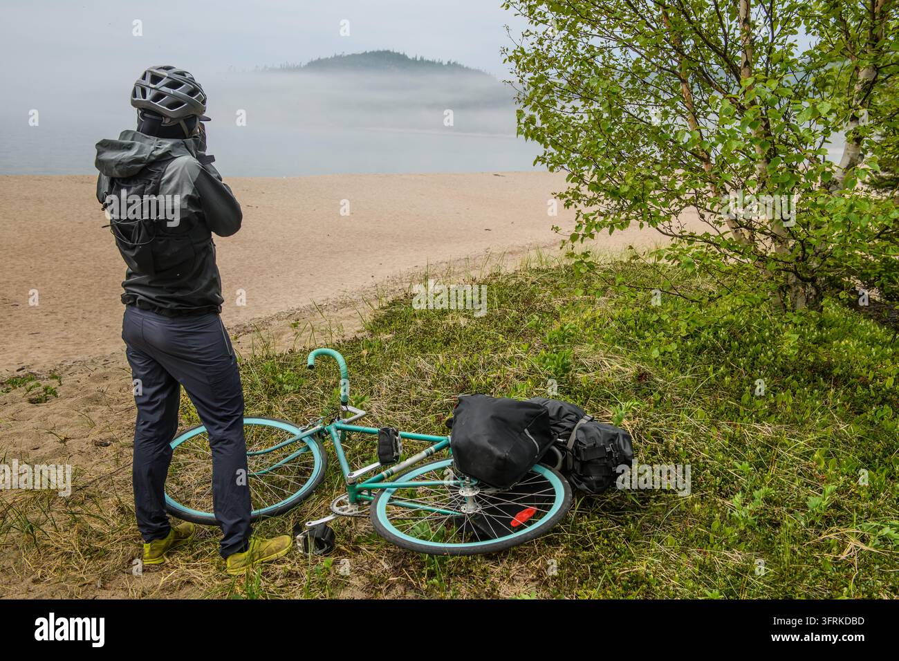 Bikepacker che si gode la vista nebbiosa da una spiaggia Foto Stock