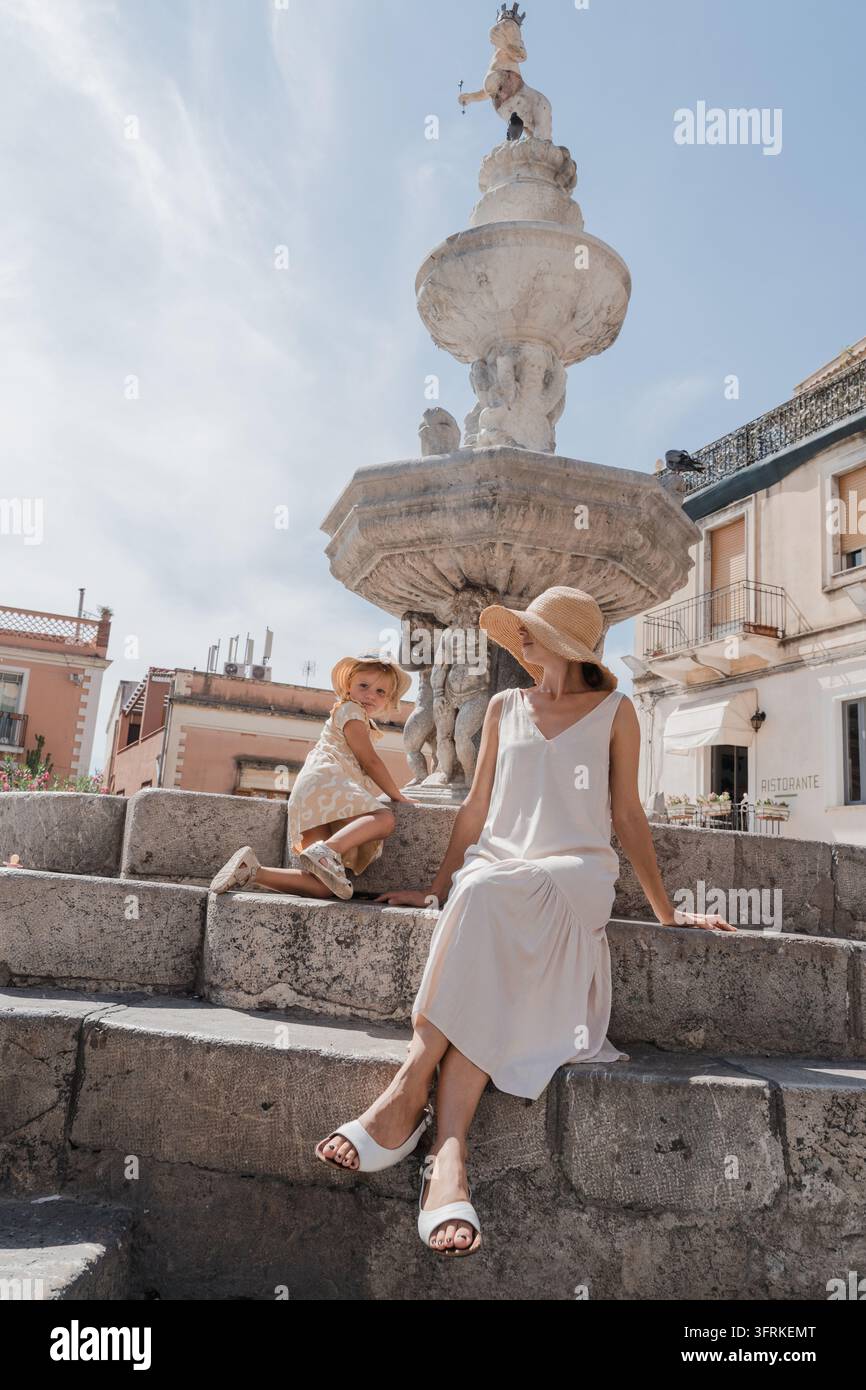 Madre e figlia sedute sui gradini di un'antica fontana europea Foto Stock